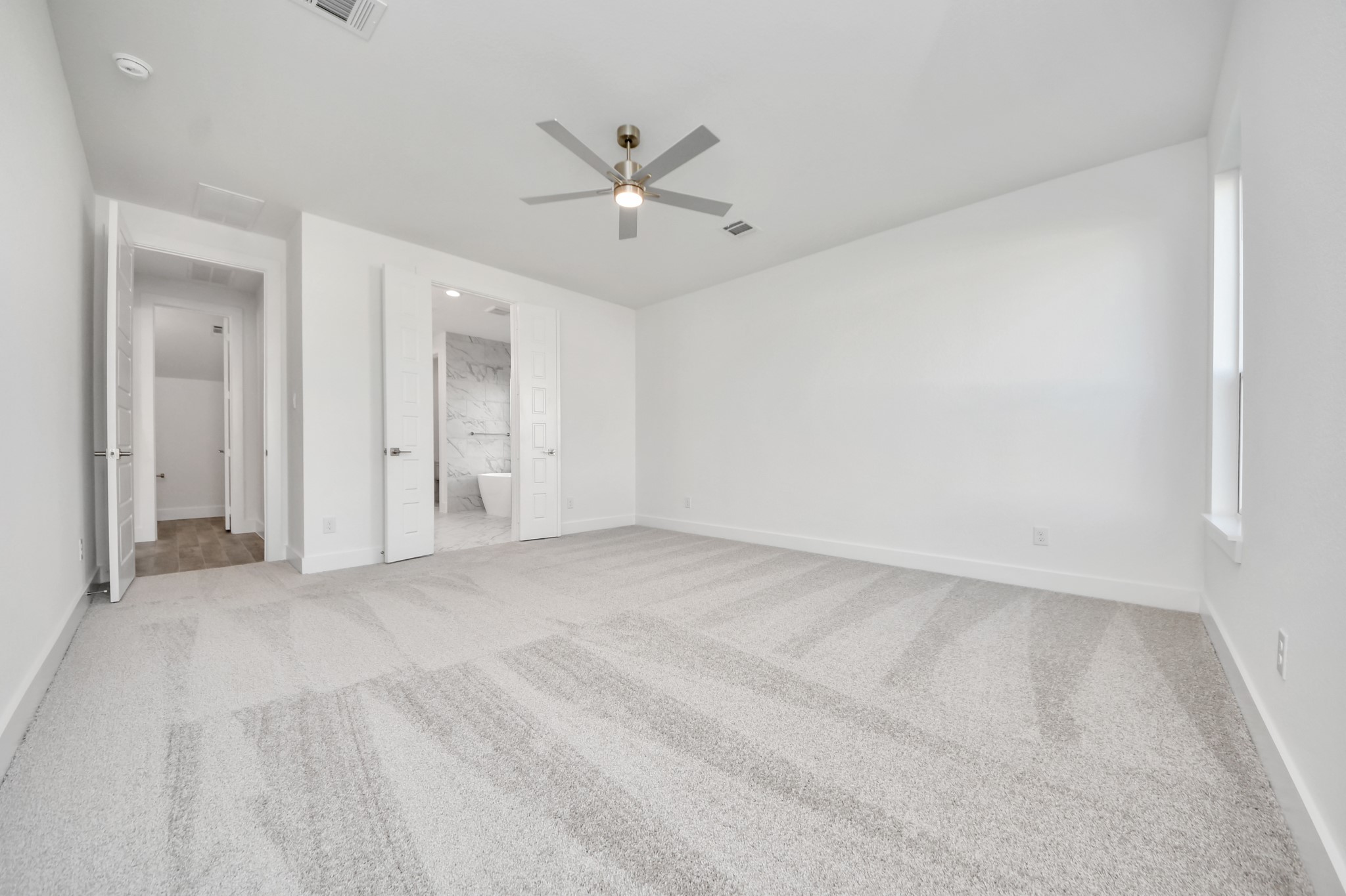 Escape and relax in the exquisite primary suite, a haven to unwind after a long day. The spacious room, located on first floor, boasts plush carpeting, soothing paint tones, high ceilings, and expansive windows adorned with privacy blinds.