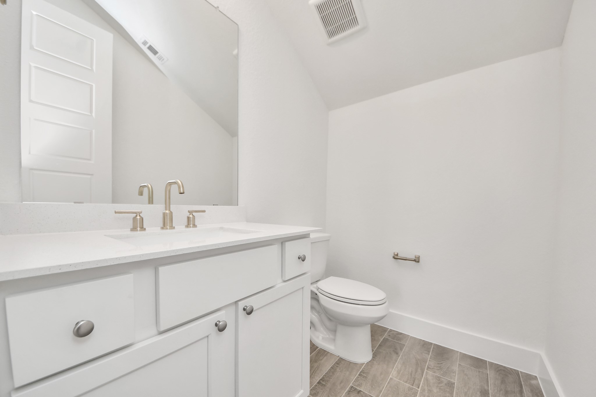 Sophisticated half bathroom adorned with contemporary finishes. The elegant 5-panel door welcomes you to a space where style meets functionality. Notice the sleek hardware accents that add a touch of modern charm. The vanity boasts light-colored countertops, beautifully complemented by a tasteful vanity light, creating a well-lit and inviting atmosphere.