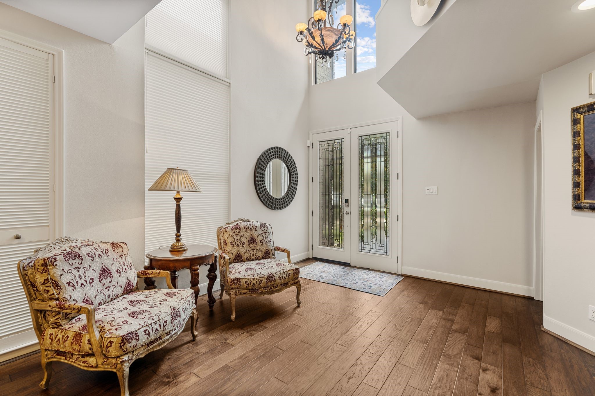 Decorative glass double doors, a soaring ceiling and high windows create a bright, welcoming foyer with space for a sitting area.