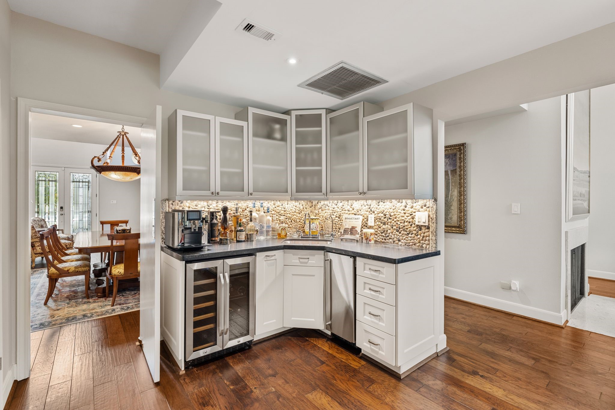 The wet bar with a sink, beverage refrigerator, illuminated pebble backsplash and glass-front cabinetry is perfectly located between the dining room and kitchen.