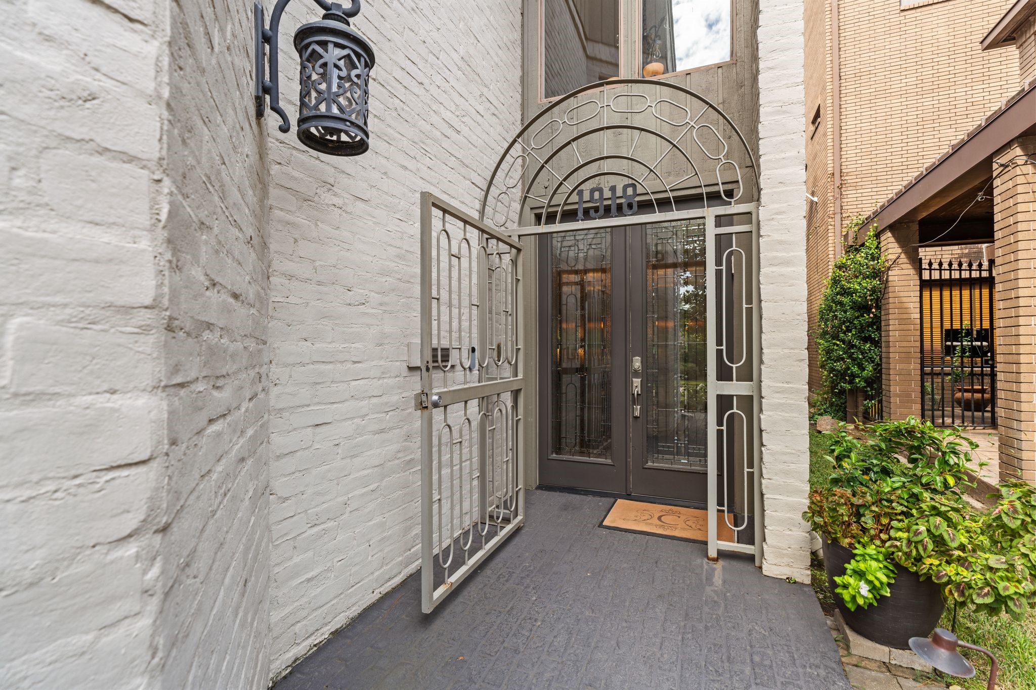 A decorative arched gate, glass double doors and lantern lighting create a distinctive entrance framed by painted brick.