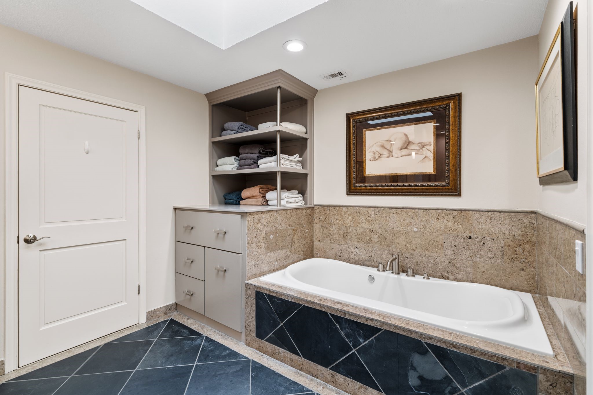 A separate soaking tub with a stone surround offers a relaxing retreat, complemented by built-in linen shelving and cabinetry.
