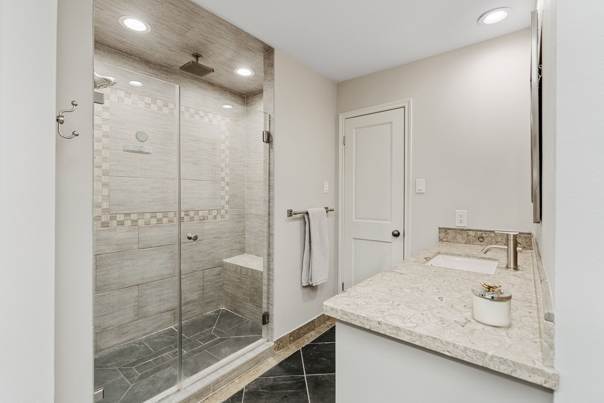 The primary bath features a spacious glass-enclosed shower with a rainfall showerhead, built-in bench and decorative tile accents.