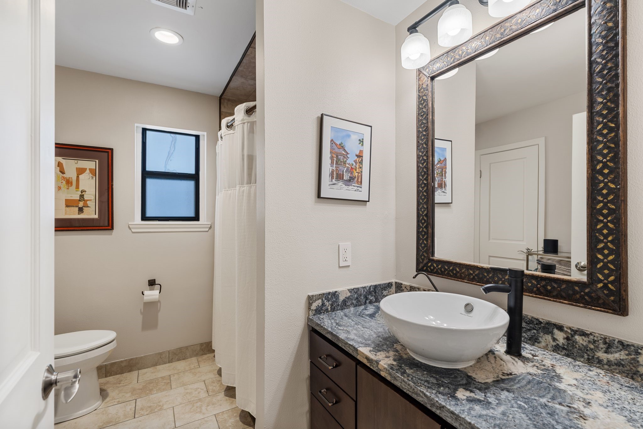 A vessel sink, striking stone countertop and decorative framed mirror give the secondary bathroom a distinctive look.