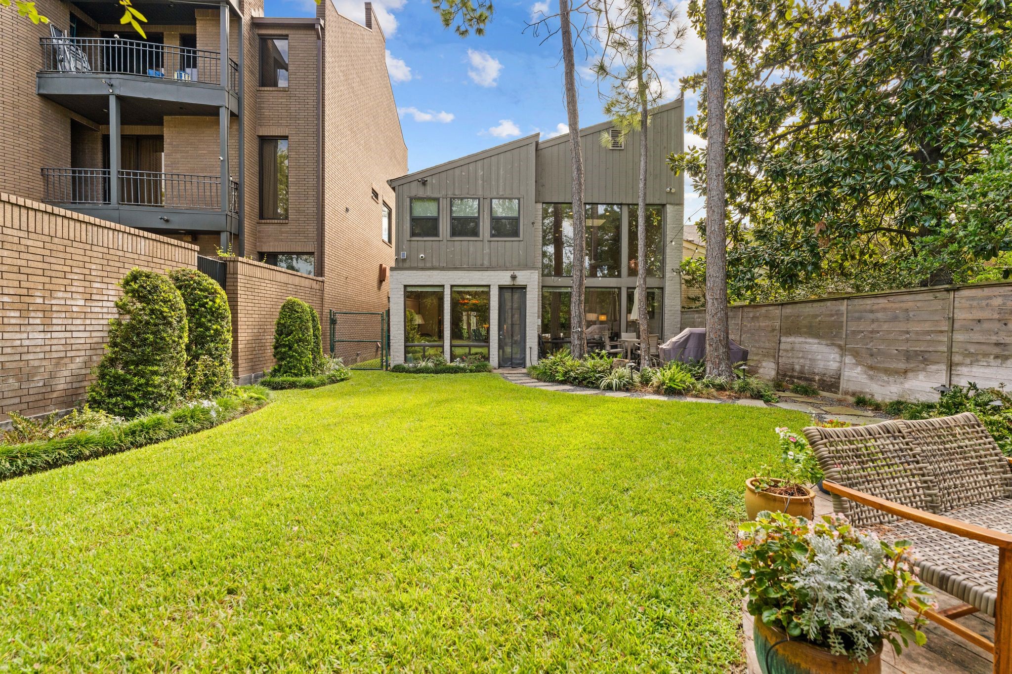 Dramatic rear windows overlook a lush lawn framed by established landscaping and tall trees. Fenced outdoor area includes adjoining county-owned land.