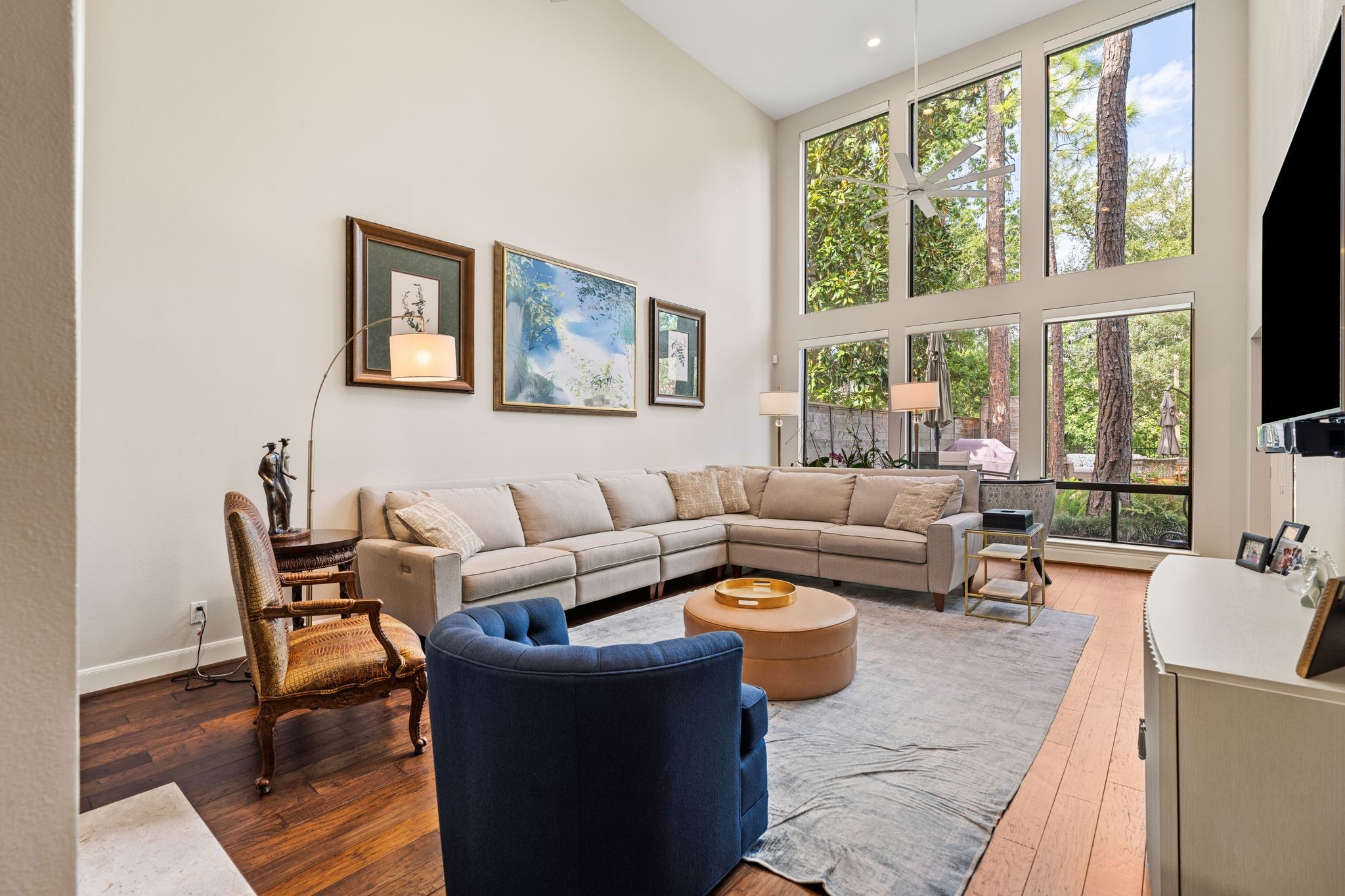 Dramatic two-story windows fill the living room with natural light and frame views of mature trees and the landscaped outdoor setting. Dramatic two-story windows fill the living room with natural light and frame views of mature trees and the landscaped outdoor setting.