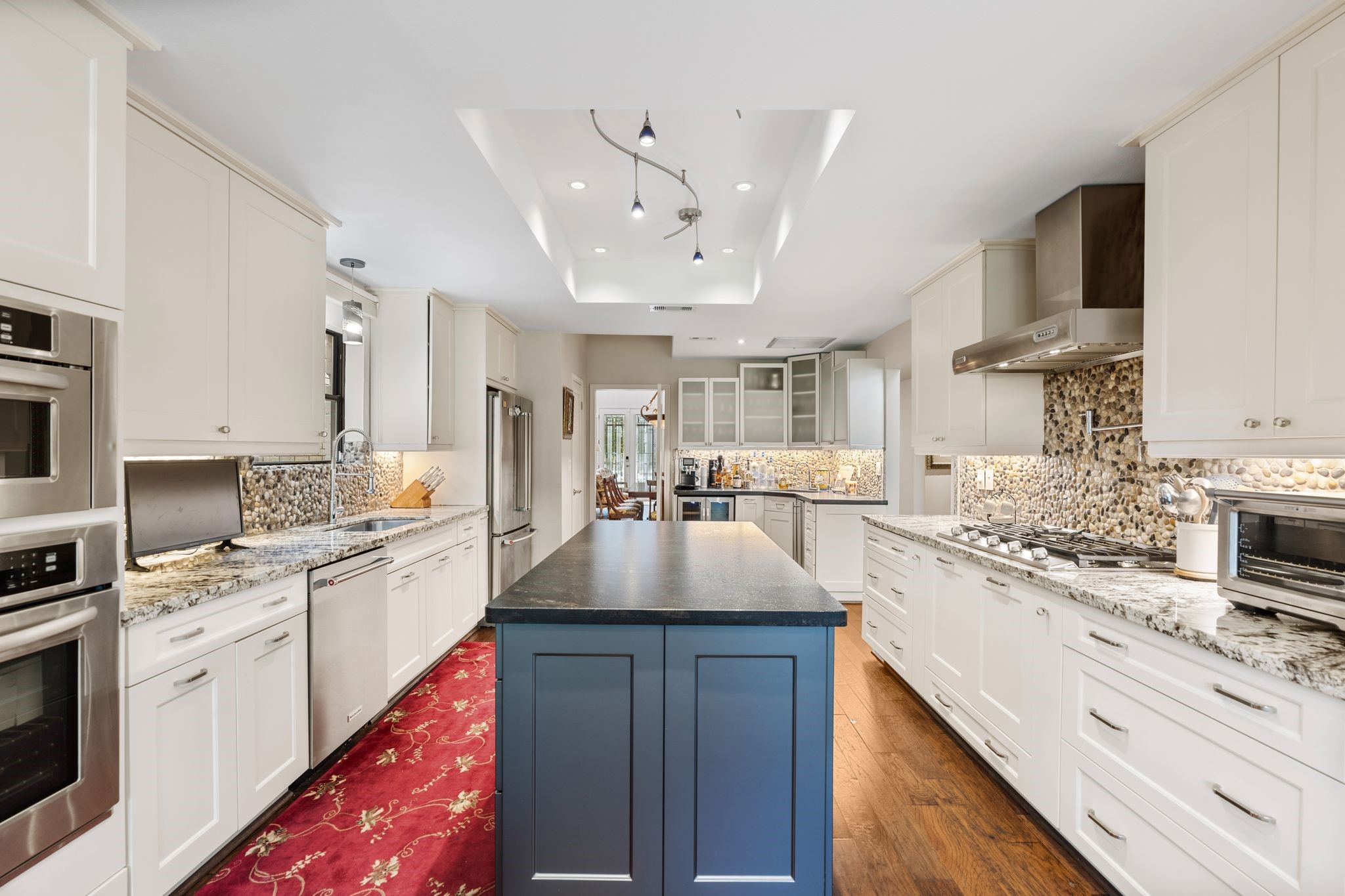 The kitchen features a contrasting blue island, granite countertops, gas cooking and a distinctive pebble backsplash, complemented by abundant white cabinetry.
