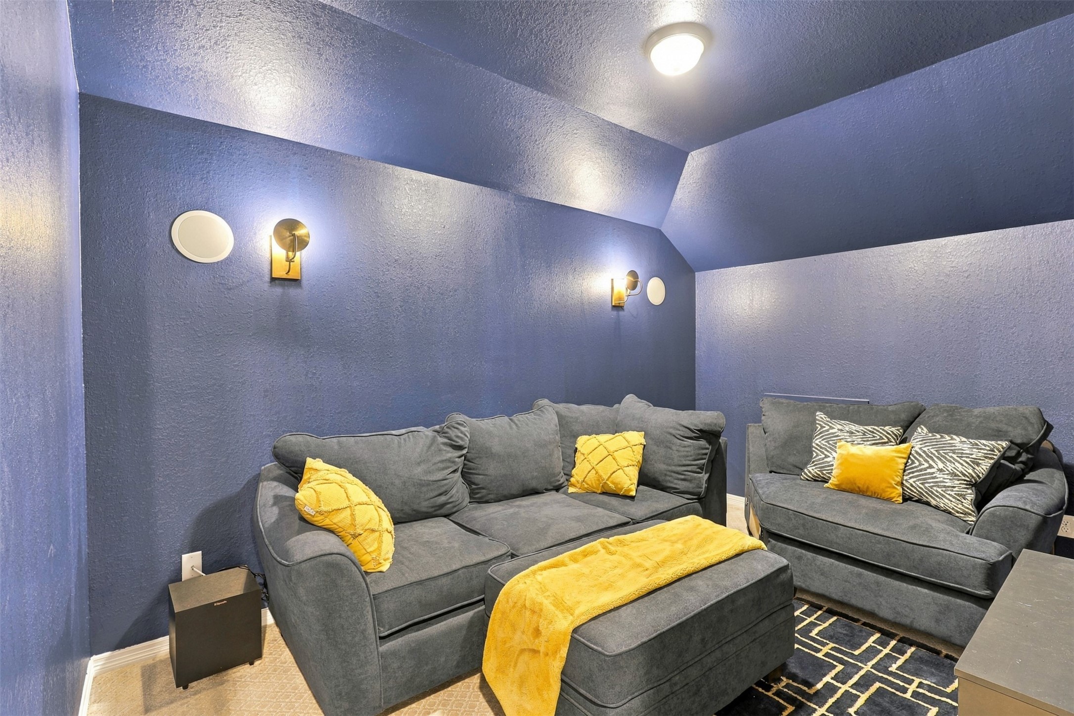 Movie night, anyone? This cozy media room features rich blue walls, comfortable sectional seating, and warm accent lighting for an inviting entertainment experience. It's the perfect spot to settle in with your favorite film, enjoy game day, or spend a relaxing evening at home.