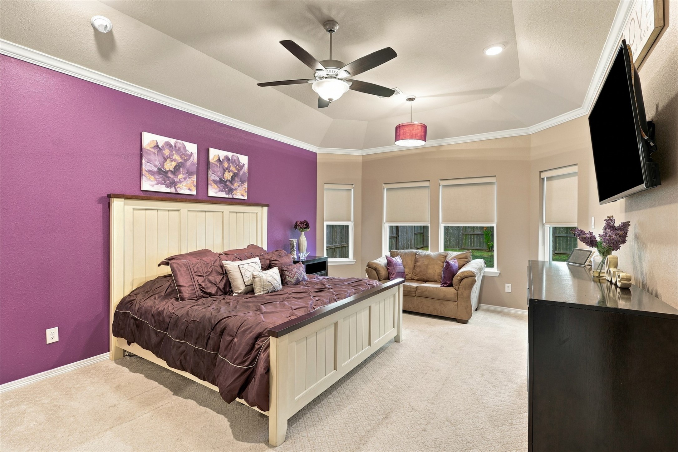 YOUR PRIVATE SLICE OF PARADISE AWAITS! Step into this BREATHTAKING primary retreat, where luxurious comfort meets stunning designer style! The gorgeous statement accent wall adds a dramatic splash of color and sophistication, while the spacious layout offers a charming sitting area perfect for curling up with your favorite book or enjoying a peaceful moment! A ceiling fan adds everyday comfort, and just LOOK at that beautiful designer carpeting!