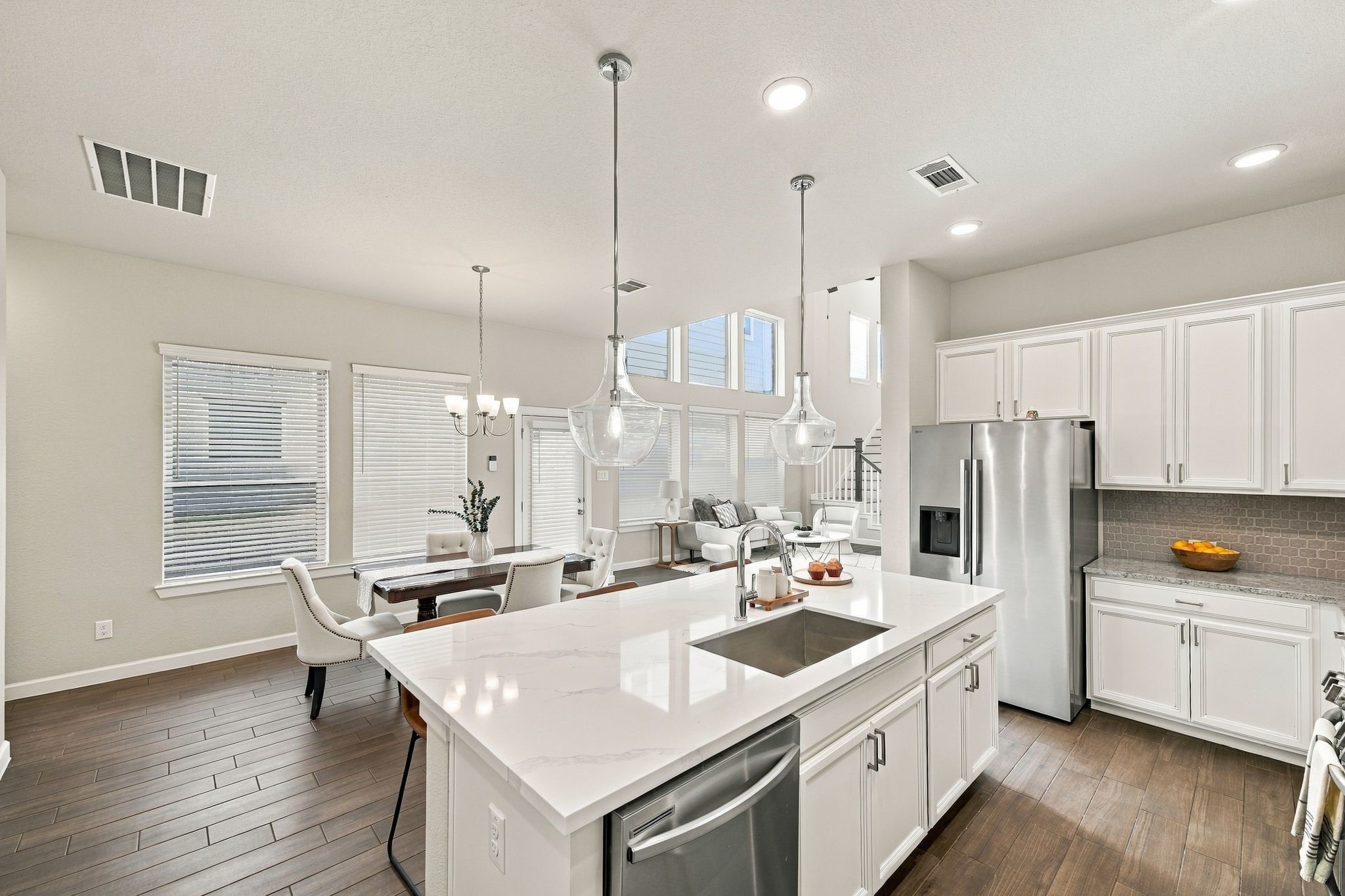 Stainless refrigerator, quartz island, dining and living room in clear view. Cooking here means never leaving the conversation.