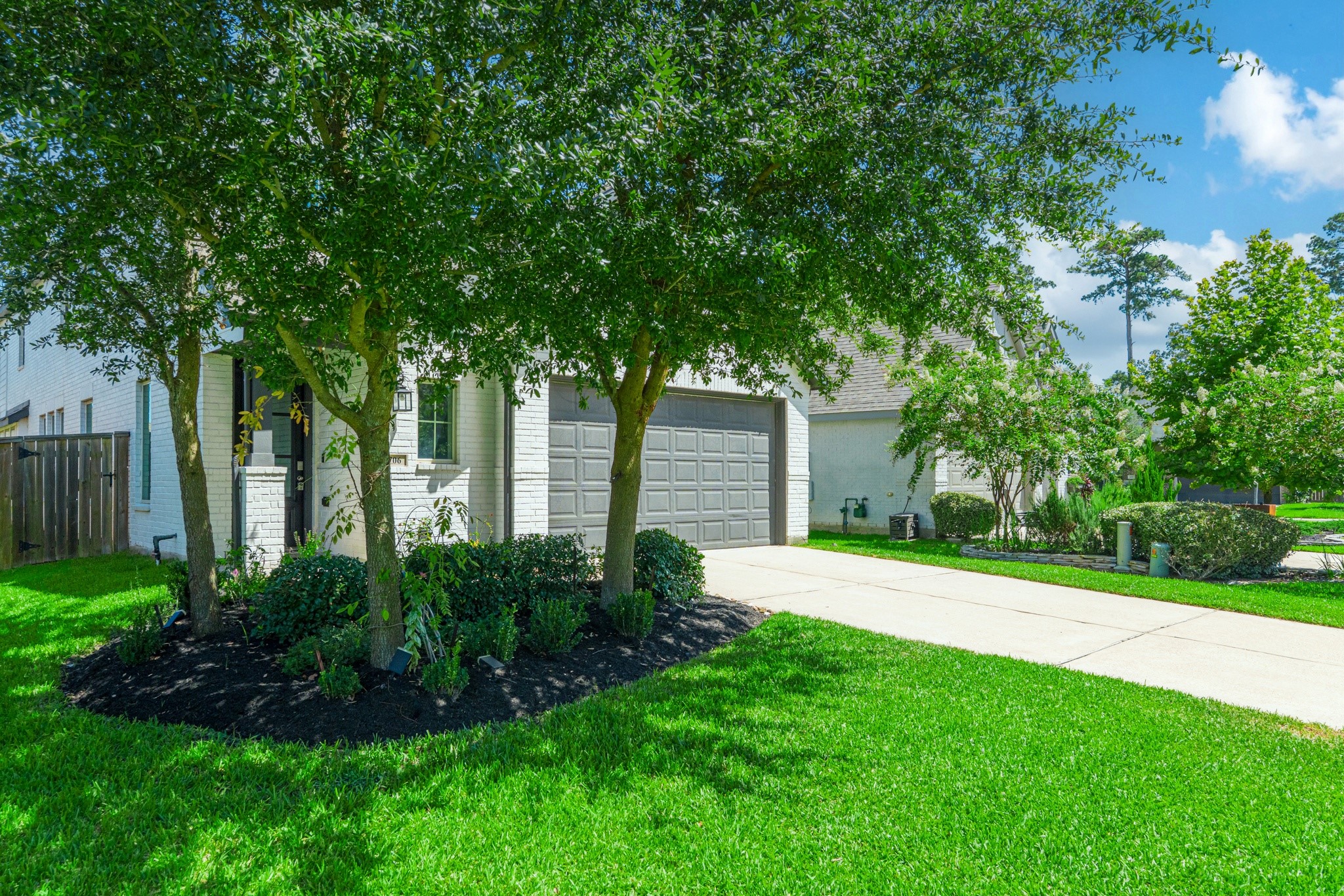 Street-level front view highlighting the home's mature trees, lush green landscaping, and wide concrete driveway leading to the attached two-car garage. This home's exterior is both welcoming and unmistakably modern  a true standout in the neighborhood.