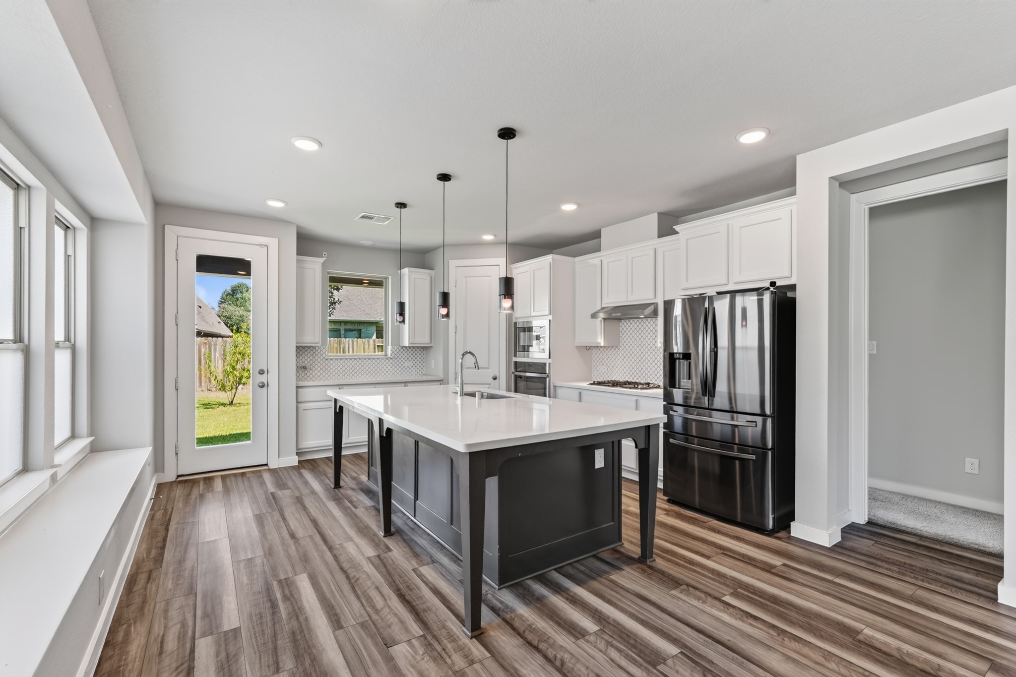 A breathtaking kitchen opens directly to the family and dining areas  featuring crisp white cabinetry, a bold navy blue island with quartz countertops, pendant lighting, and stainless steel appliances. This kitchen was designed to impress every single day.