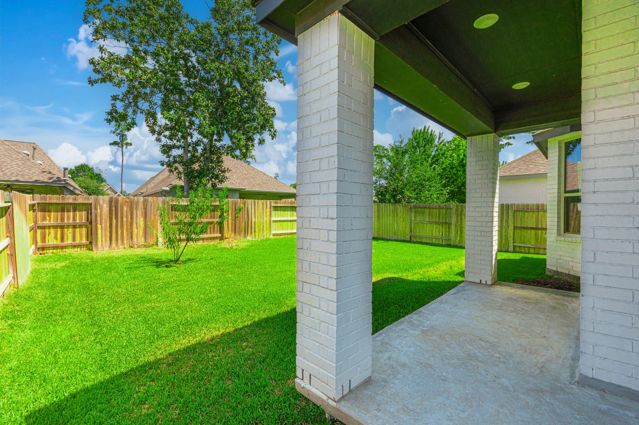 The covered back patio is your private outdoor retreat  white columns, a generous concrete pad, and a shaded overhead structure invite you to enjoy morning coffee, evening meals, and weekend gatherings just steps from the kitchen in total comfort.