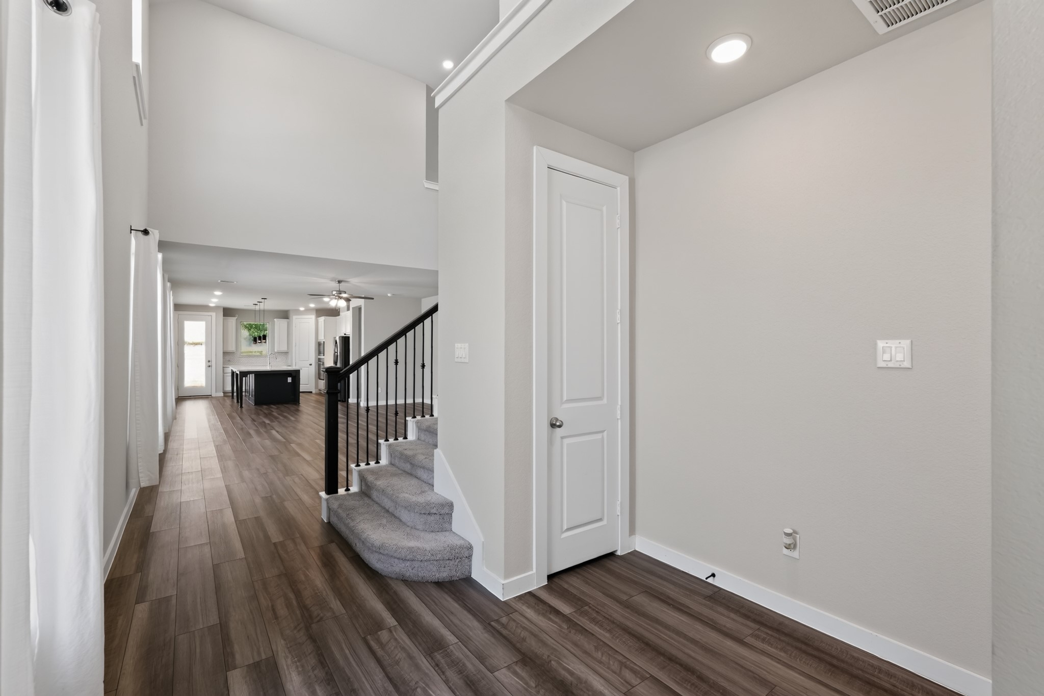 Step inside to a bright, open entry foyer featuring gorgeous dark hardwood-style flooring, soaring ceilings, and crisp neutral walls. The staircase visible in the background adds immediate architectural elegance to this light-filled and spacious entryway.