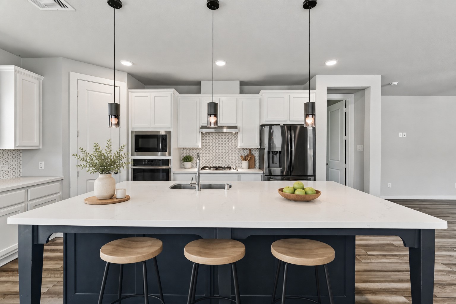 The kitchen's oversized island is the centerpiece  a brilliant white quartz countertop atop a striking navy blue base, surrounded by pendant lighting overhead. Ample seating and generous prep space make this stunning island the true heart of the home.