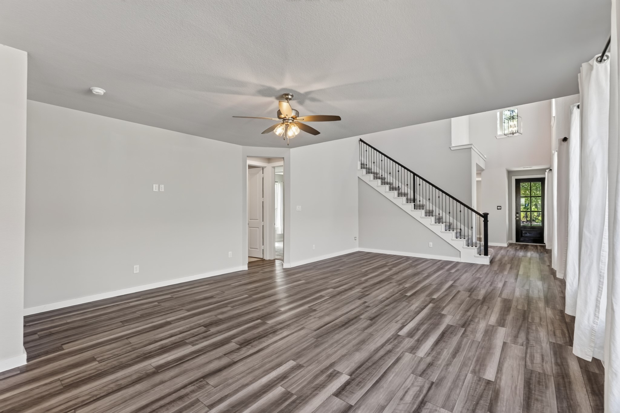 The family room's open-concept design allows beautiful sight lines across the living, dining, and kitchen areas, with the elegant black iron stair railing adding striking visual interest. Dark hardwood floors and a ceiling fan complete the polished look.