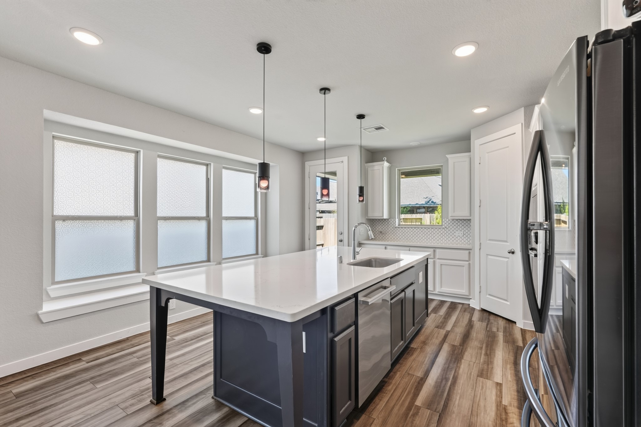 Natural light pours in through the kitchen window, illuminating the white quartz island, stainless appliances, and the open layout beyond. The view from here perfectly captures the home's seamless and beautifully designed open-concept floor plan.