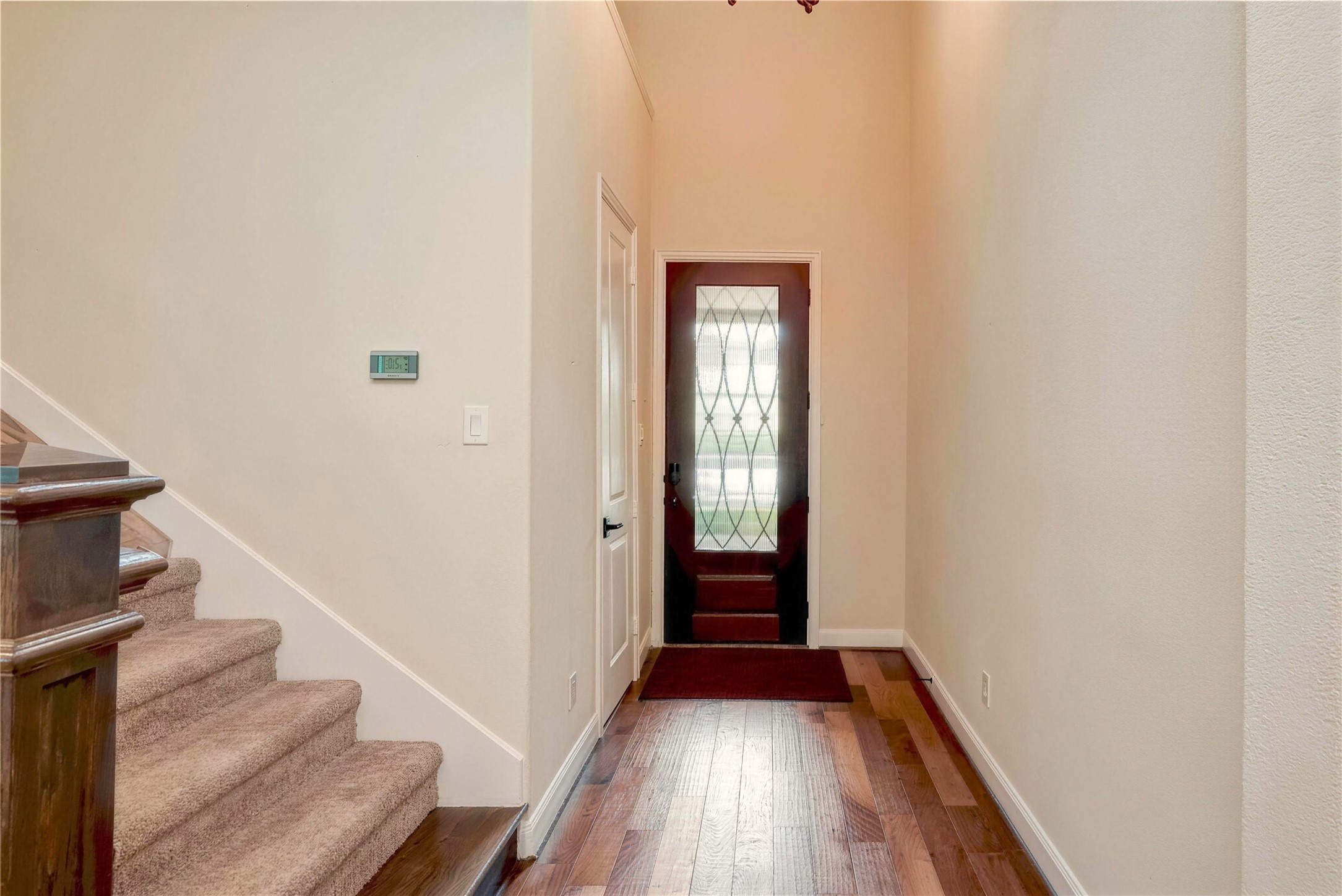 Inviting entryway featuring a stylish glass-paneled front door, warm hardwood floors, and a carpeted staircase leading to the upper level.