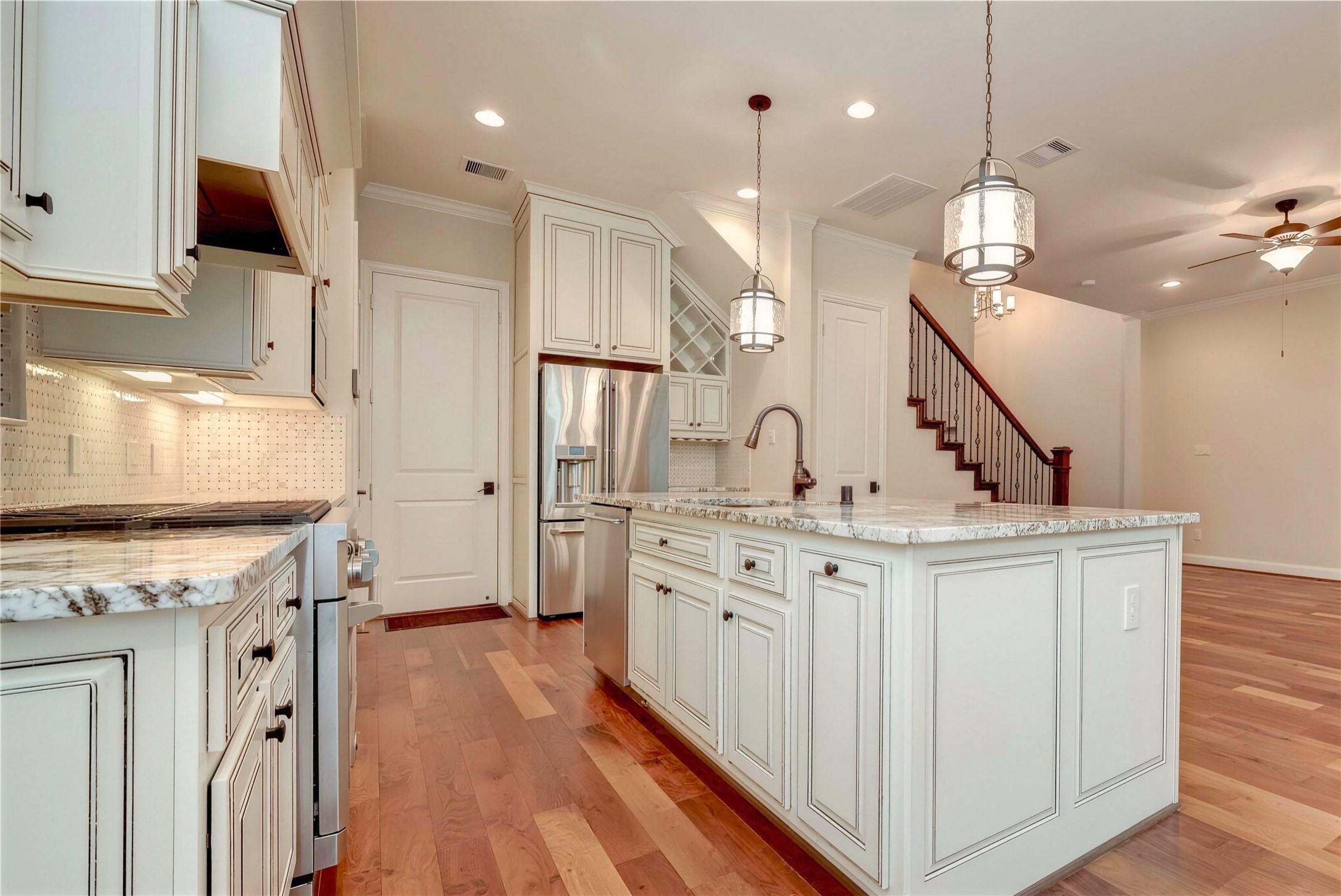 Elegant kitchen featuring granite countertops, stainless steel appliances, and pendant lighting, seamlessly connecting to a living area with hardwood floors and a stylish staircase.