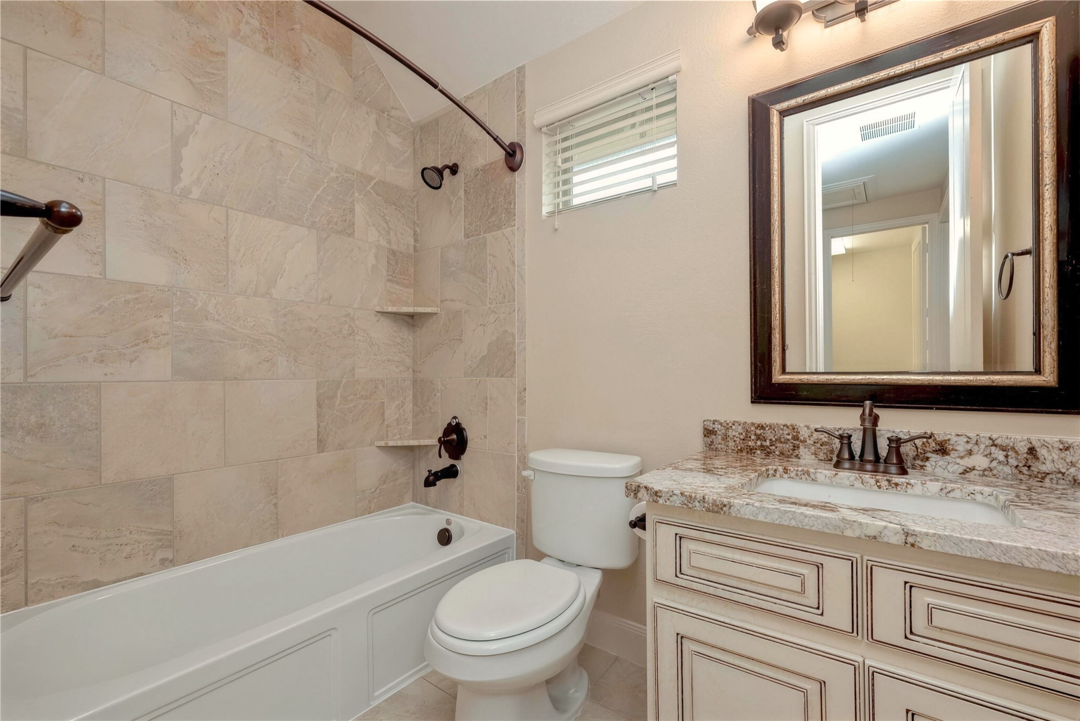 Elegant bathroom featuring a luxurious granite countertop, classic vanity, and a beautifully tiled shower and tub combination.