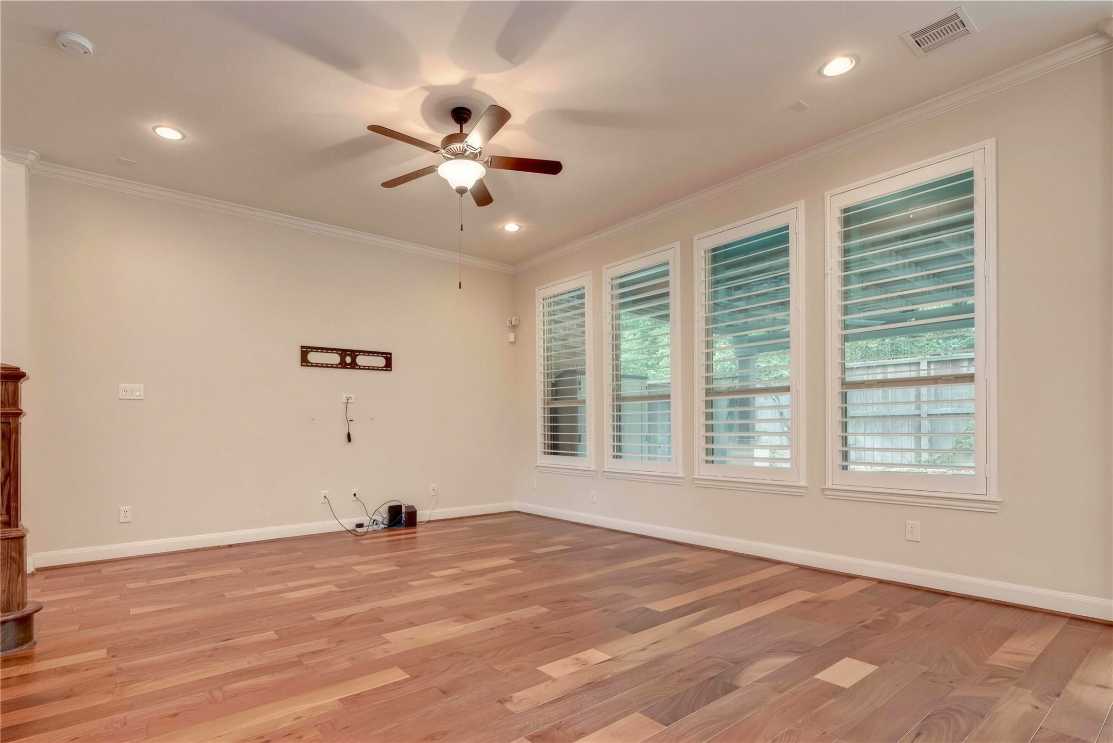 Spacious living area with rich hardwood flooring, large windows with plantation shutters, and a ceiling fan for added comfort.