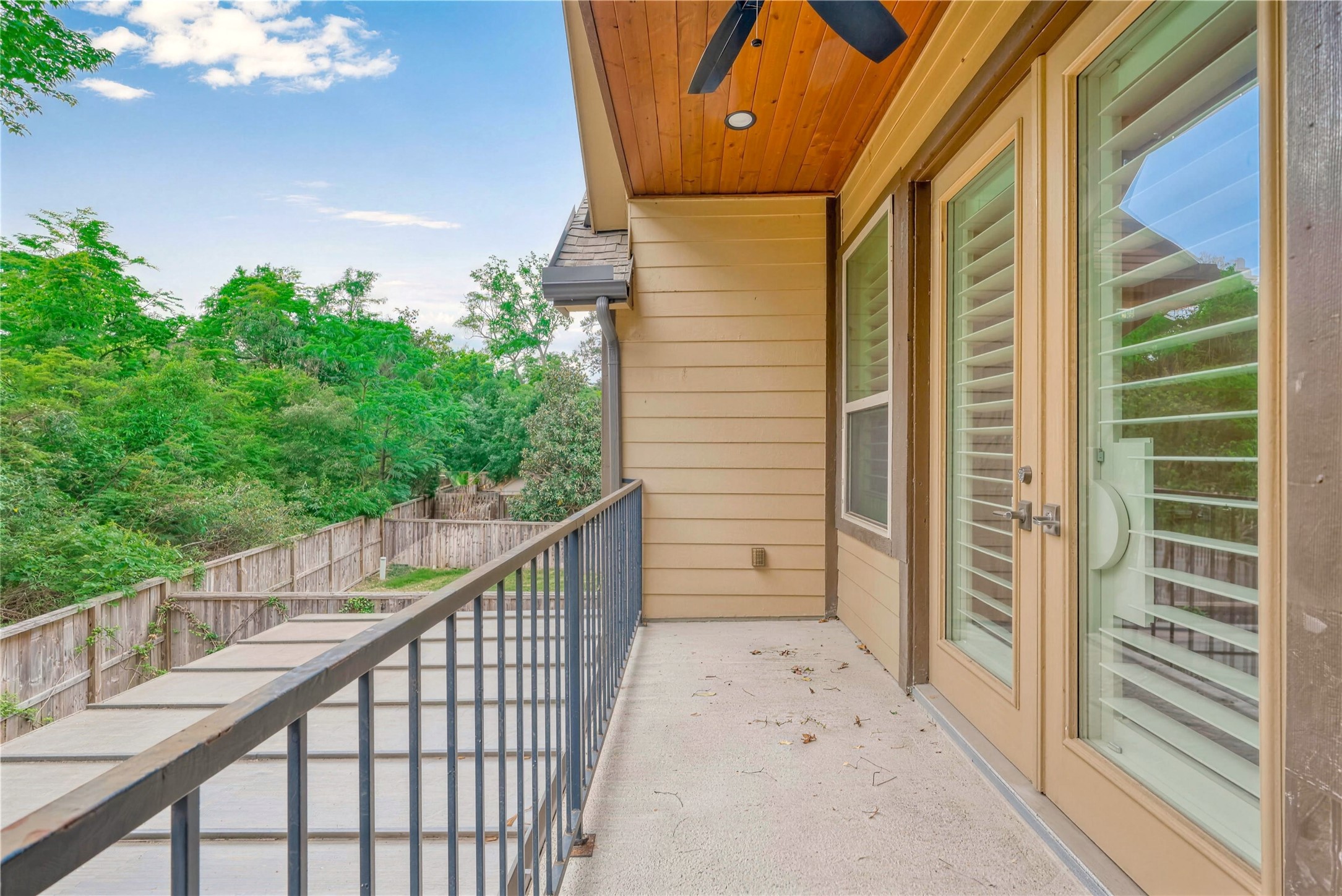 Charming balcony with French doors and a ceiling fan, offering a serene view of lush greenery for ultimate relaxation.