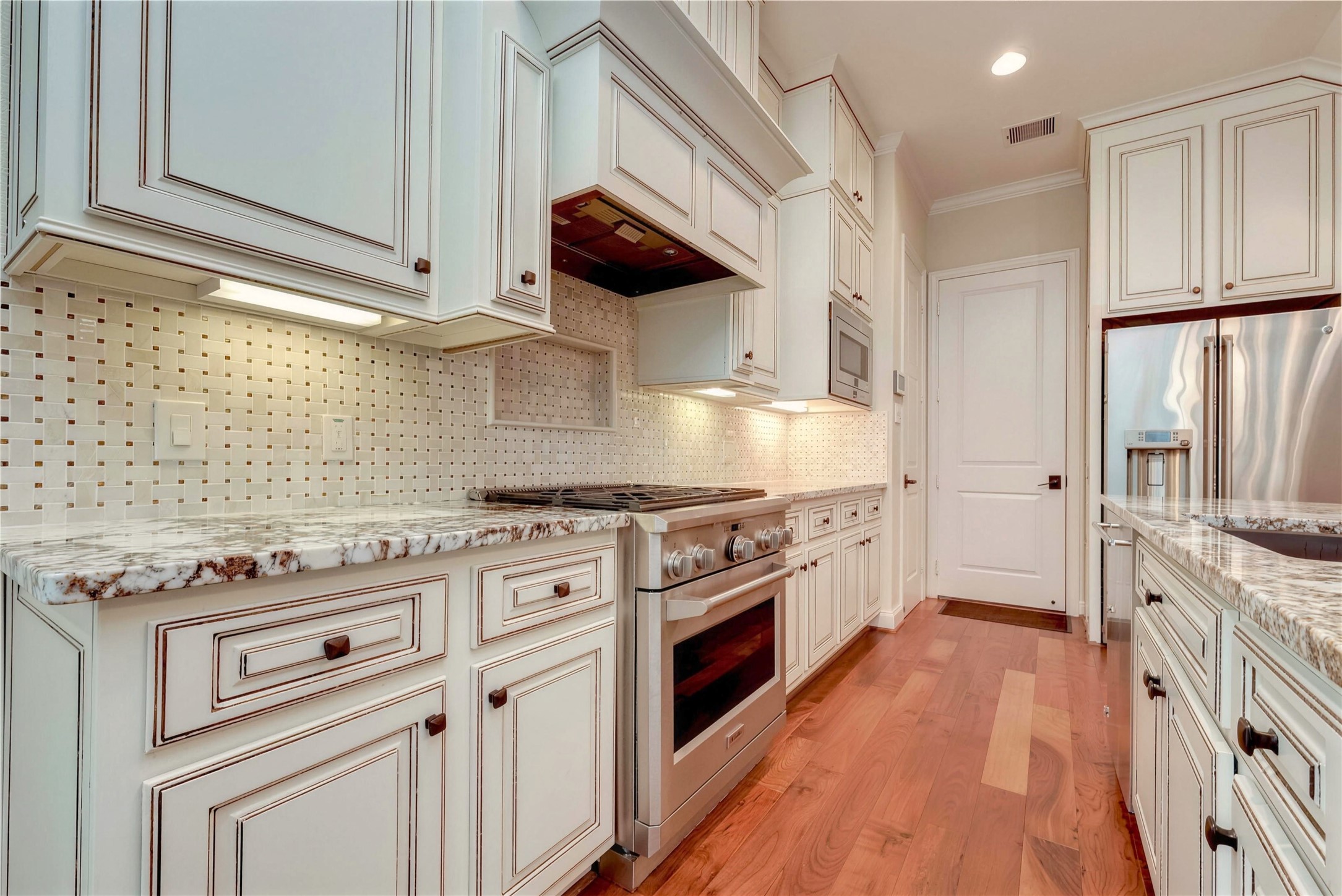 Elegant kitchen with custom cabinetry, granite countertops, and modern stainless steel appliances, complemented by a stylish backsplash and warm wood flooring.