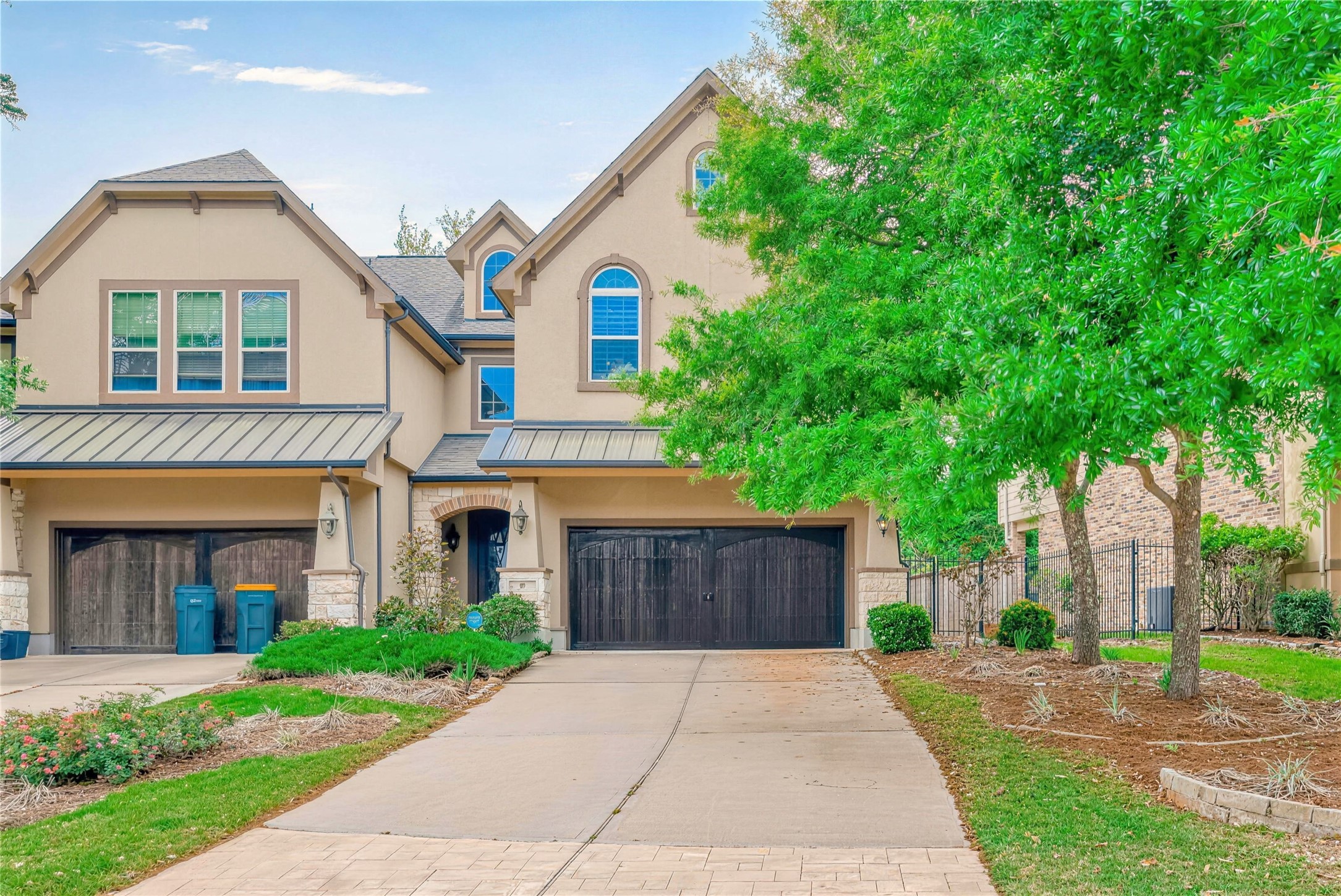 Charming two-story home with elegant arched windows and a spacious driveway leading to an attached garage, accented by lush greenery and a well-maintained front yard.