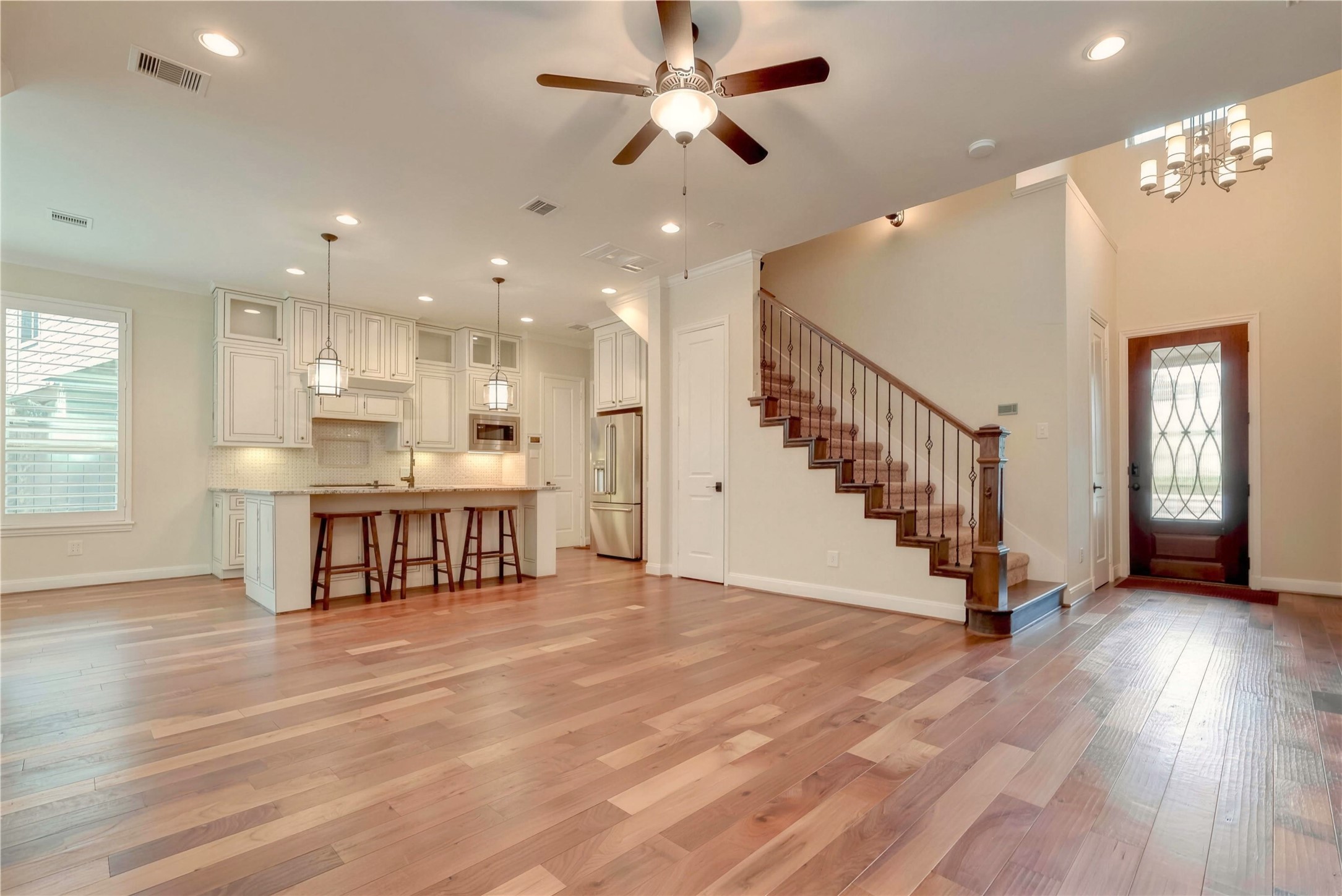 Spacious open-concept living area with elegant hardwood floors, a modern kitchen featuring white cabinetry and stainless steel appliances, and a stylish staircase leading to the upper level.