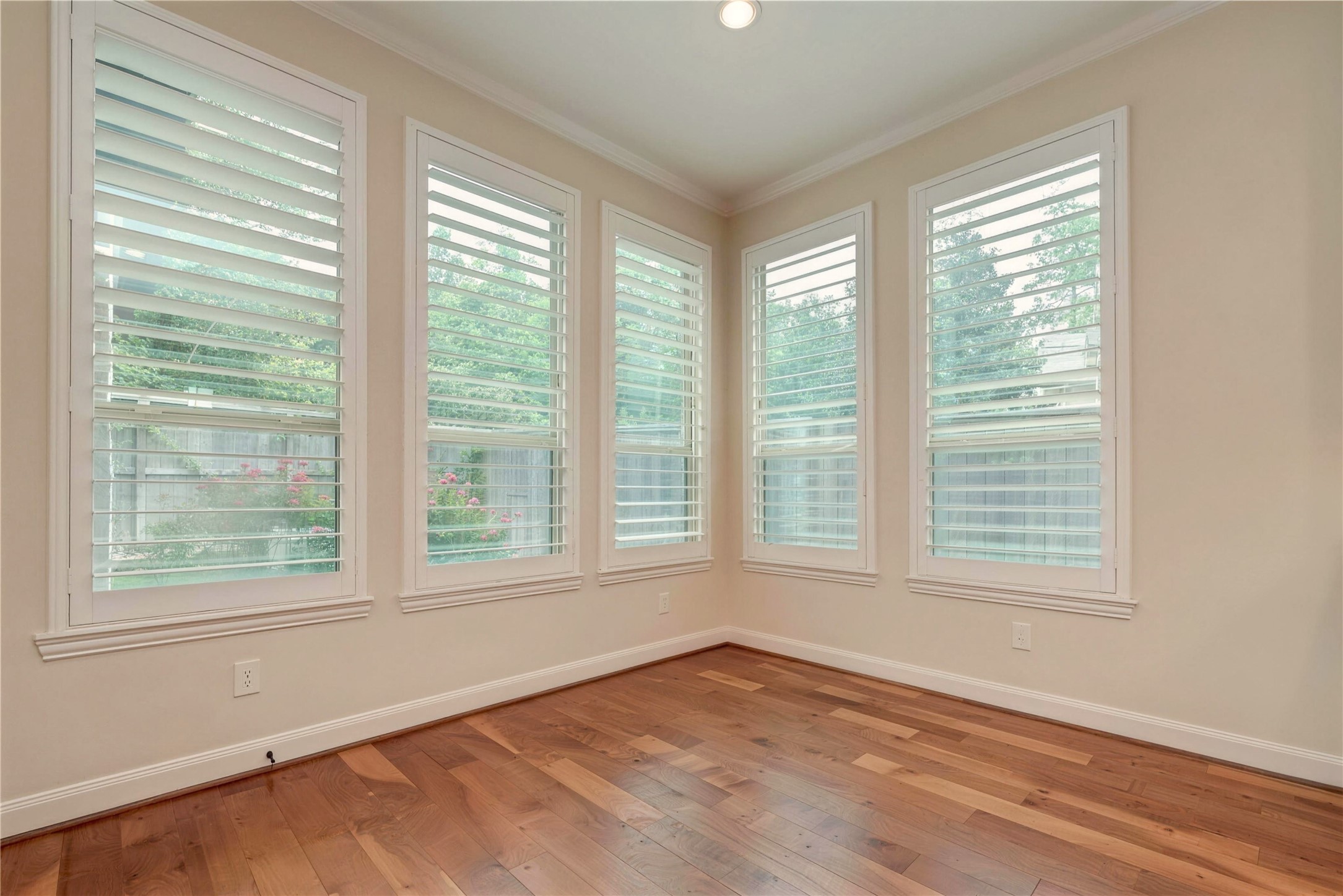 Bright and inviting space with large windows featuring plantation shutters, offering plenty of natural light and a view of the garden.