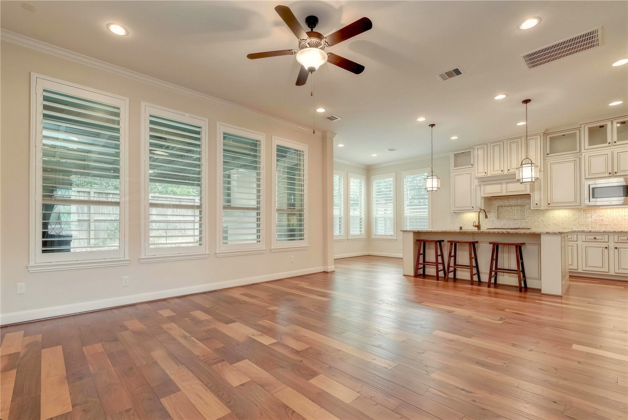 Spacious open-plan living area with rich hardwood floors, abundant natural light from large windows, and a modern kitchen featuring elegant cabinetry, a large island with seating, and stylish pendant lighting.