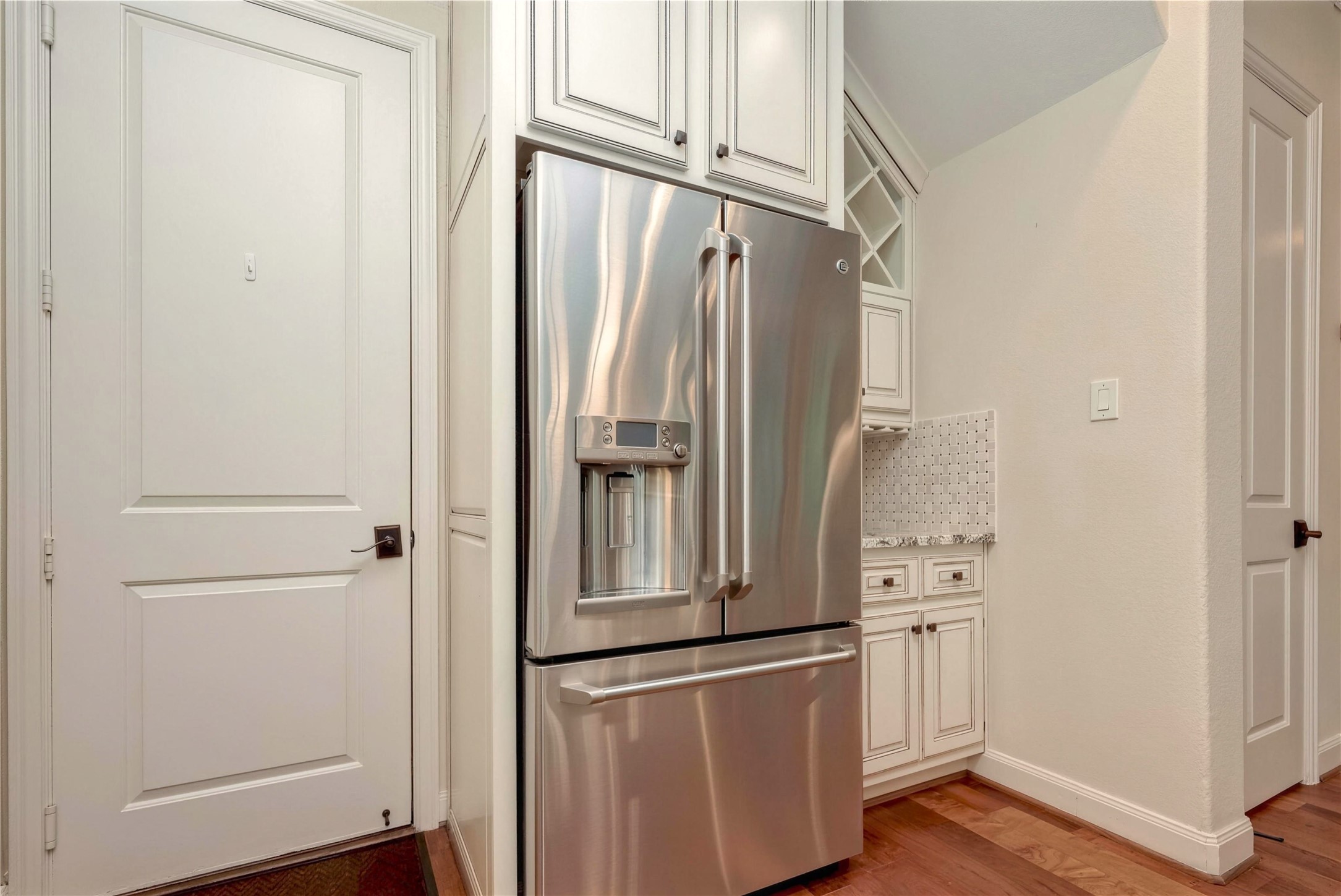 Elegant kitchen corner featuring a sleek stainless steel refrigerator, complemented by white cabinetry and a stylish tile backsplash for a modern touch.