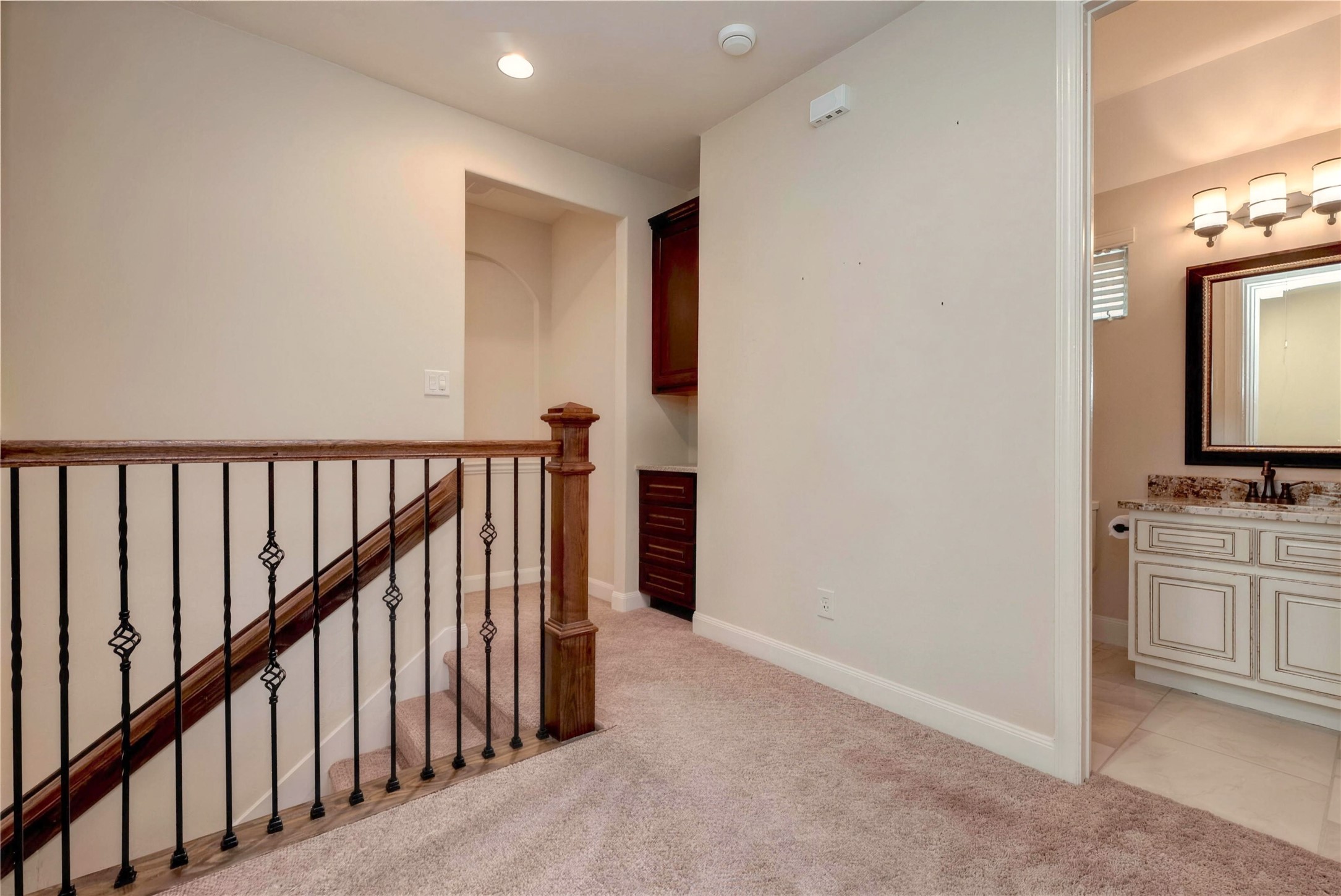 Charming upstairs landing featuring a cozy carpeted space, elegant wooden railing, and convenient access to a well-appointed bathroom with stylish fixtures.