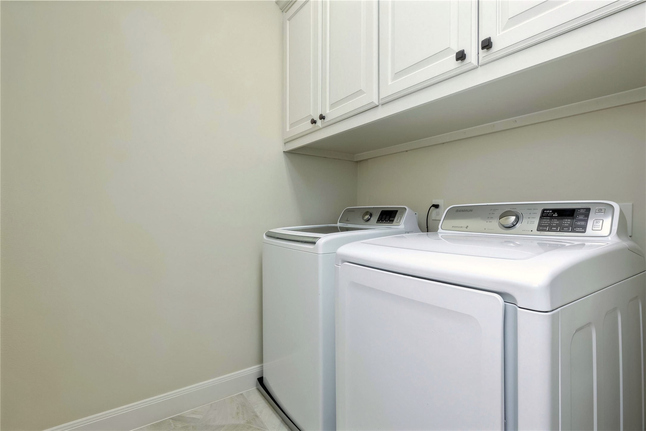 Spacious laundry room featuring modern washer and dryer, ample cabinet storage, and sleek tile flooring.