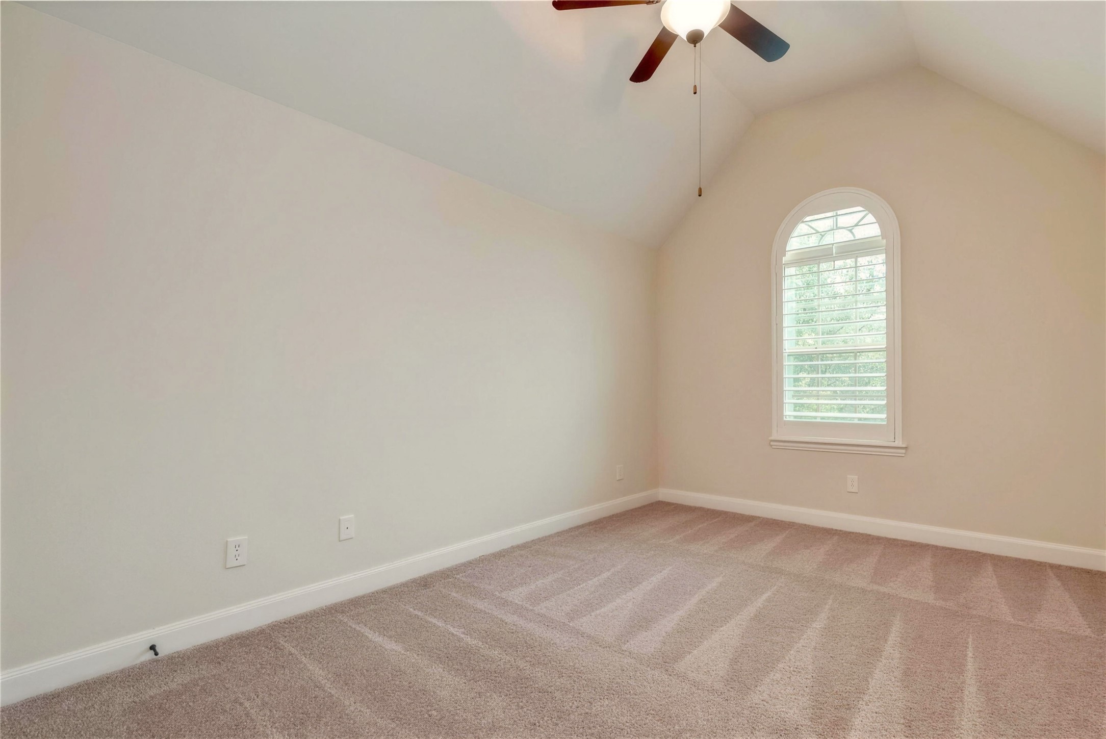 Bright and airy bedroom with vaulted ceiling, neutral carpeting, and a charming arched window offering plenty of natural light.