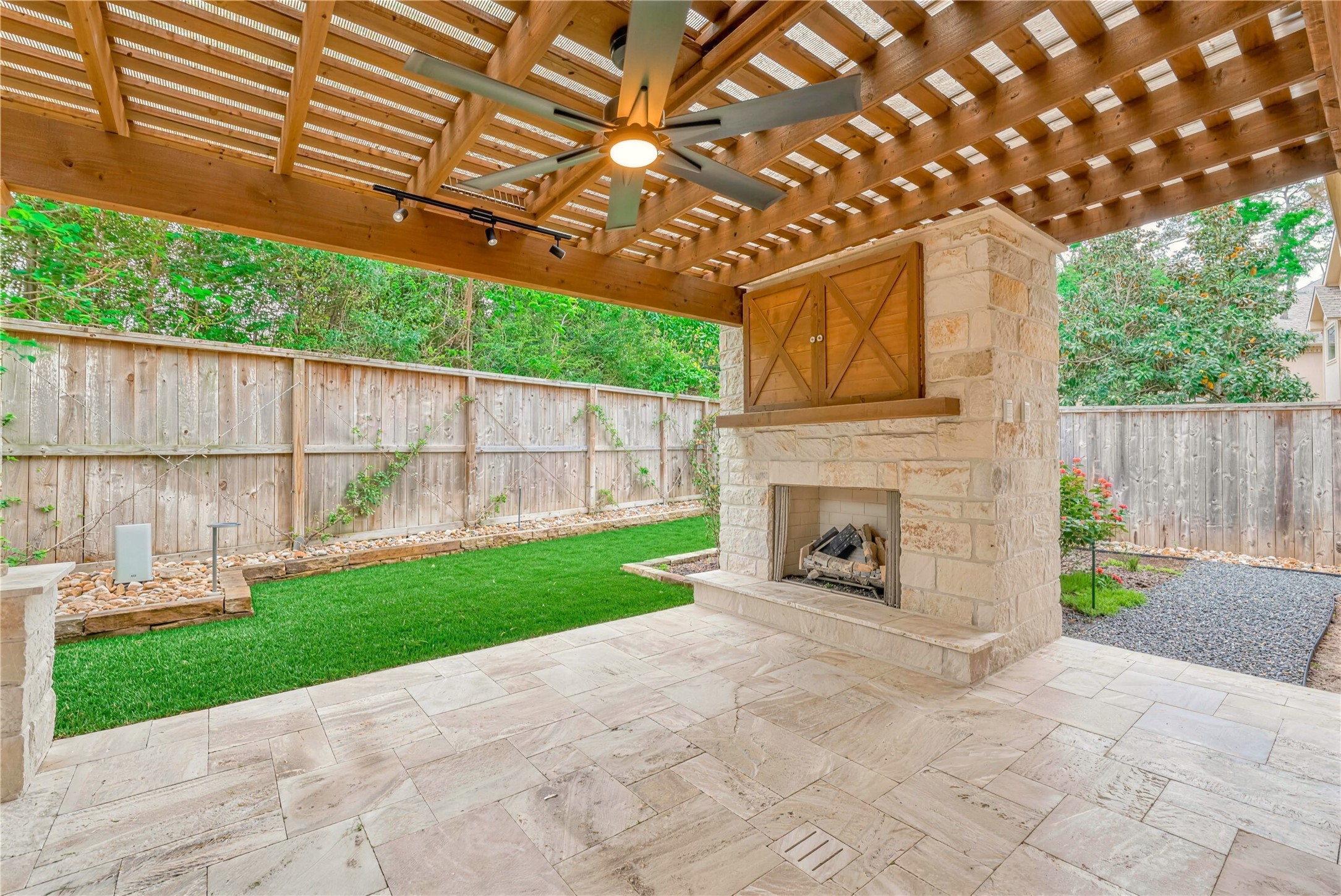 Charming outdoor patio featuring a rustic pergola, cozy stone fireplace, and beautifully landscaped garden.