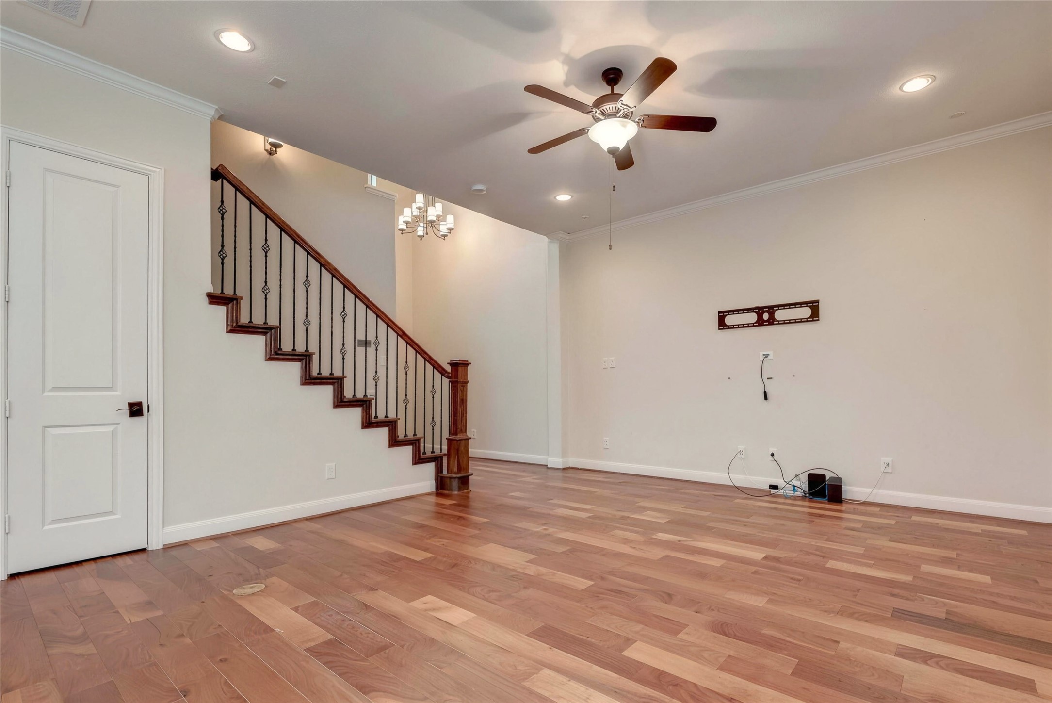 Spacious living area featuring elegant hardwood floors, a ceiling fan, and a stylish staircase with wrought iron balusters.