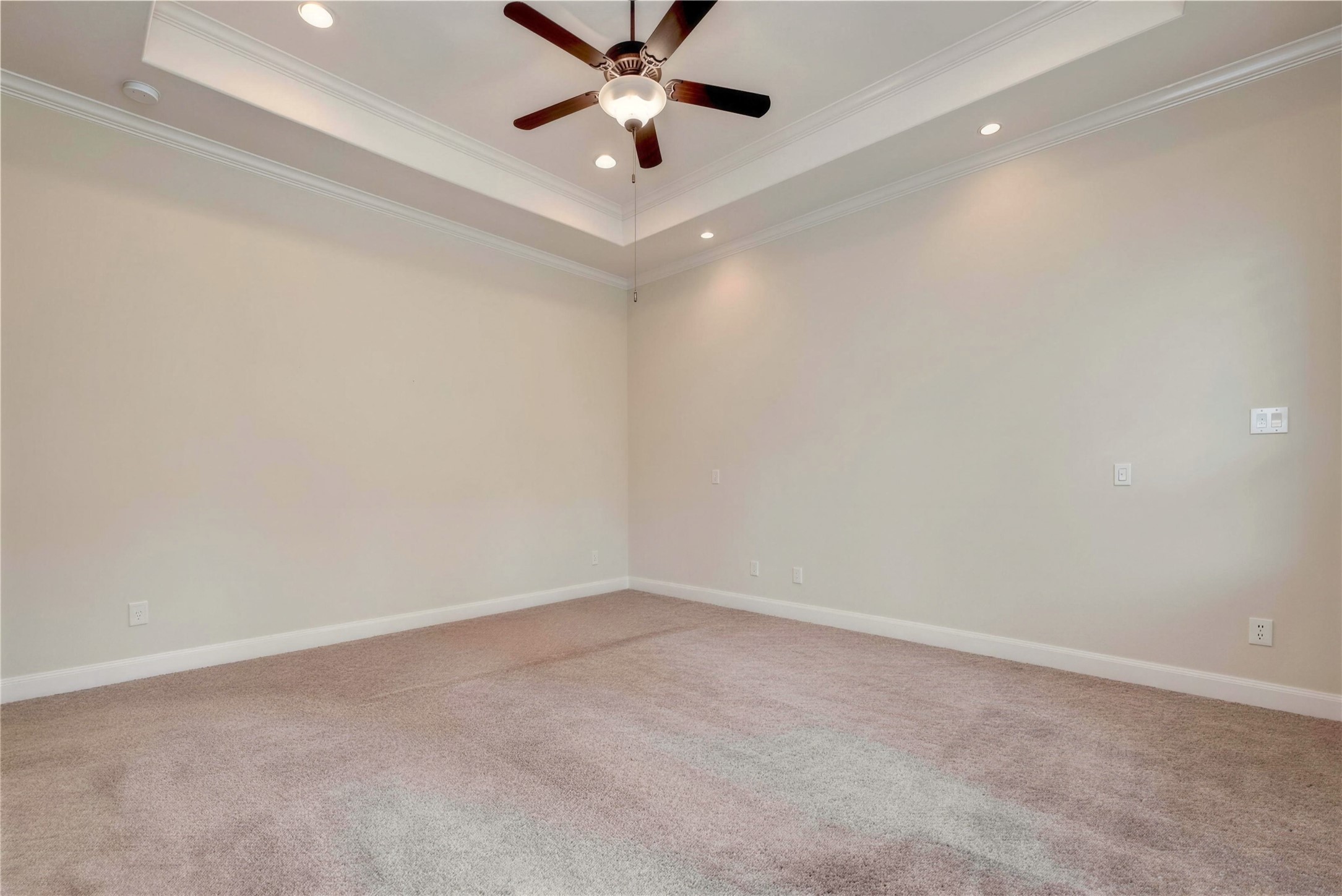Spacious room featuring a tray ceiling with recessed lighting and a ceiling fan, complemented by soft carpet flooring and neutral walls.
