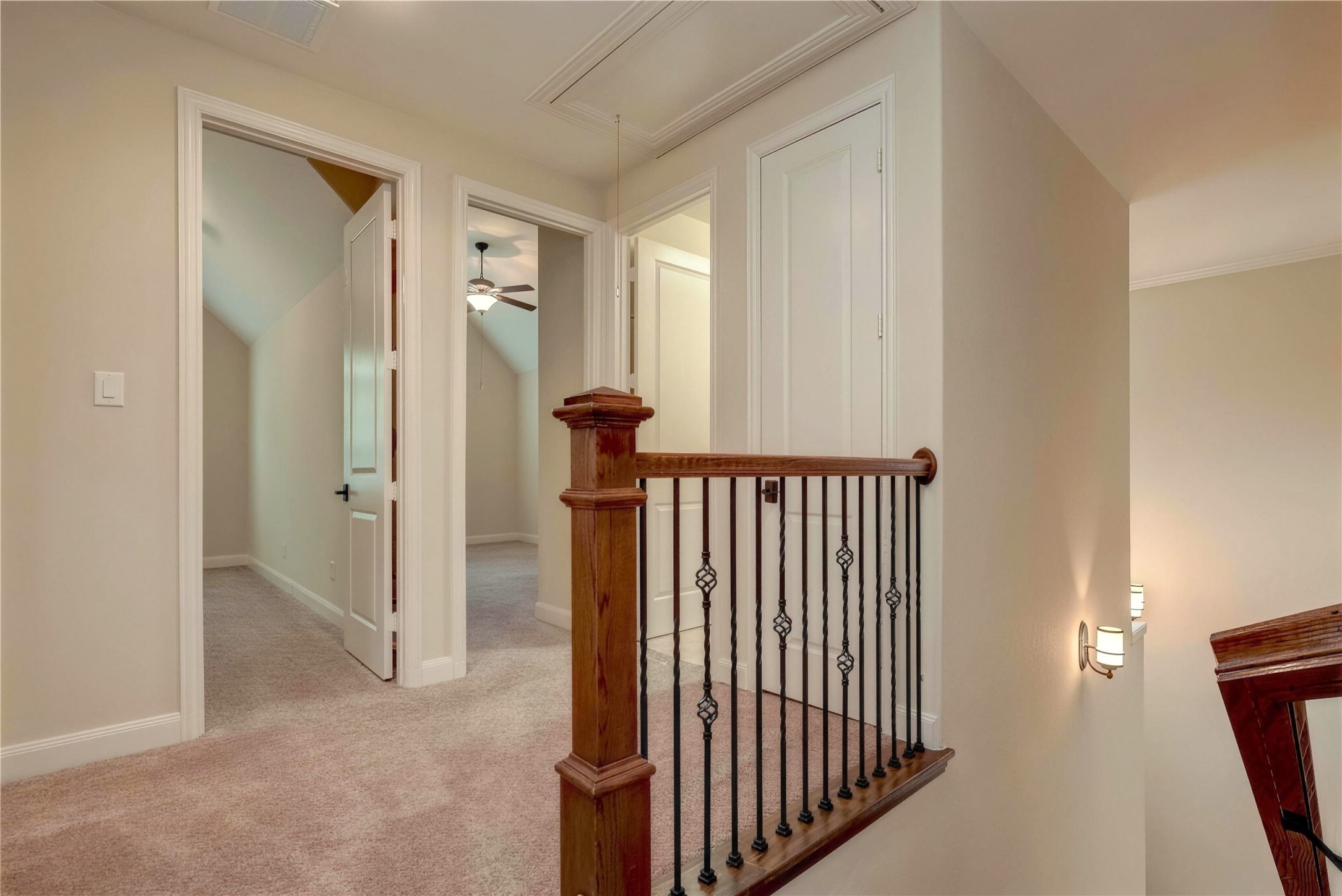 Charming upstairs landing with plush carpeting, featuring elegant wood and iron railings, and access to multiple rooms with a cozy ambiance.