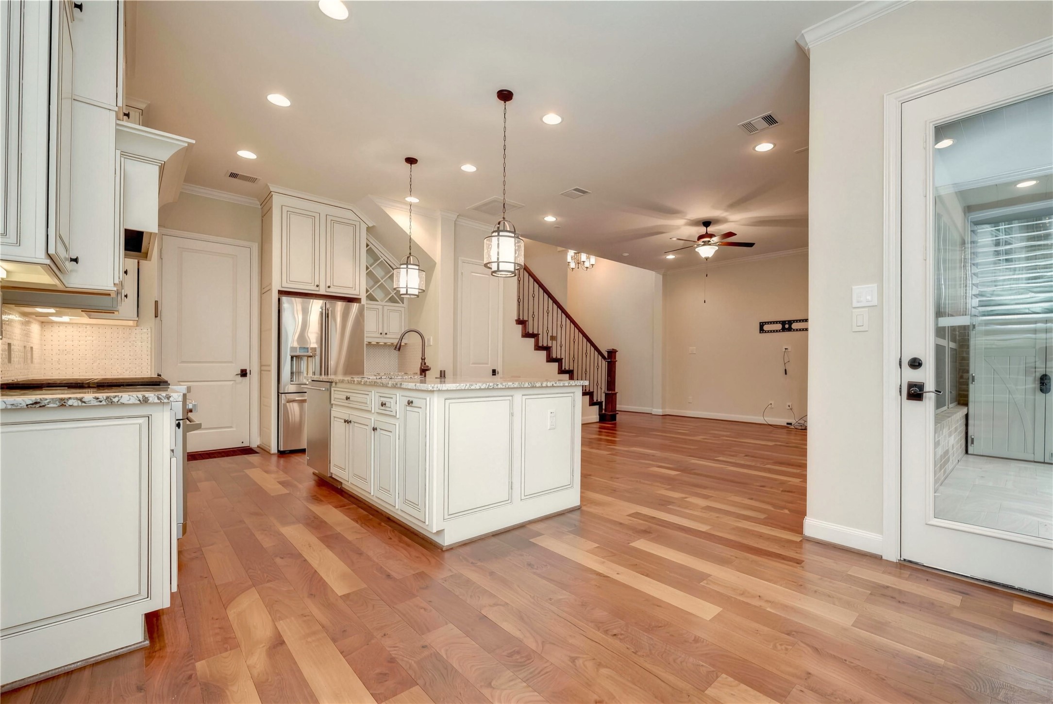 Elegant open-concept kitchen and living area featuring hardwood floors, a central island with pendant lighting, and stainless steel appliances.