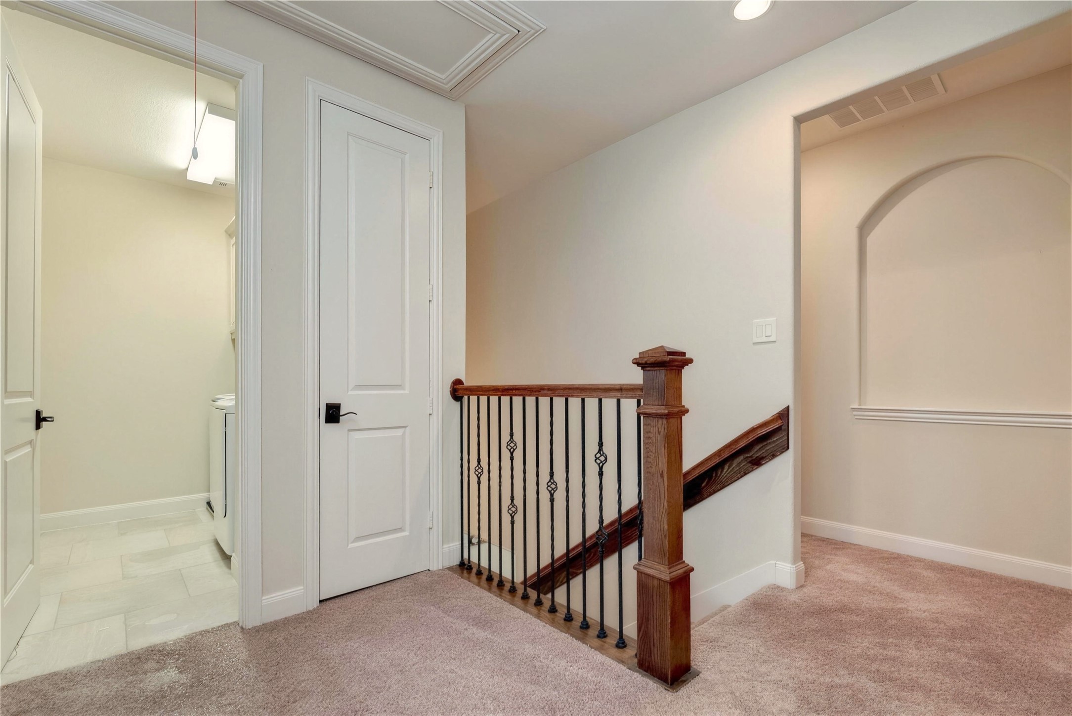 Charming hallway with plush carpeting, elegant wooden banister, and convenient access to a laundry room, perfect for seamless living.