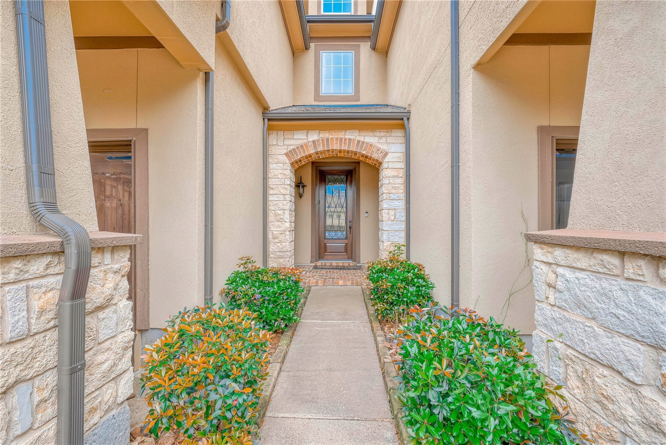 Inviting entryway with a charming arched doorway, framed by elegant stonework and lush greenery, leading to a welcoming front door.