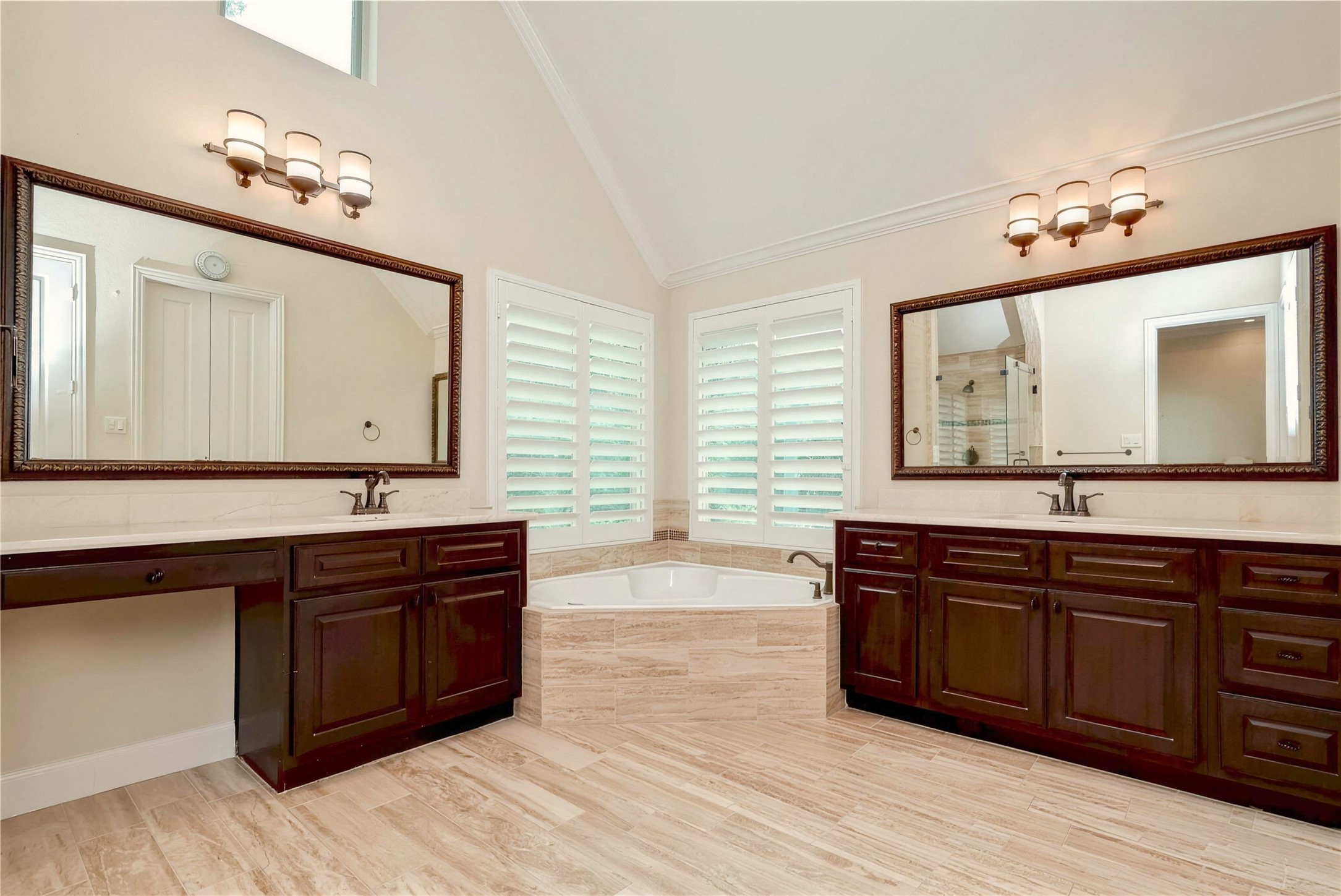 Luxurious bathroom featuring dual vanities with elegant dark wood cabinetry, a spacious corner bathtub, and stylish lighting, all accented by large mirrors and natural light from shuttered windows.