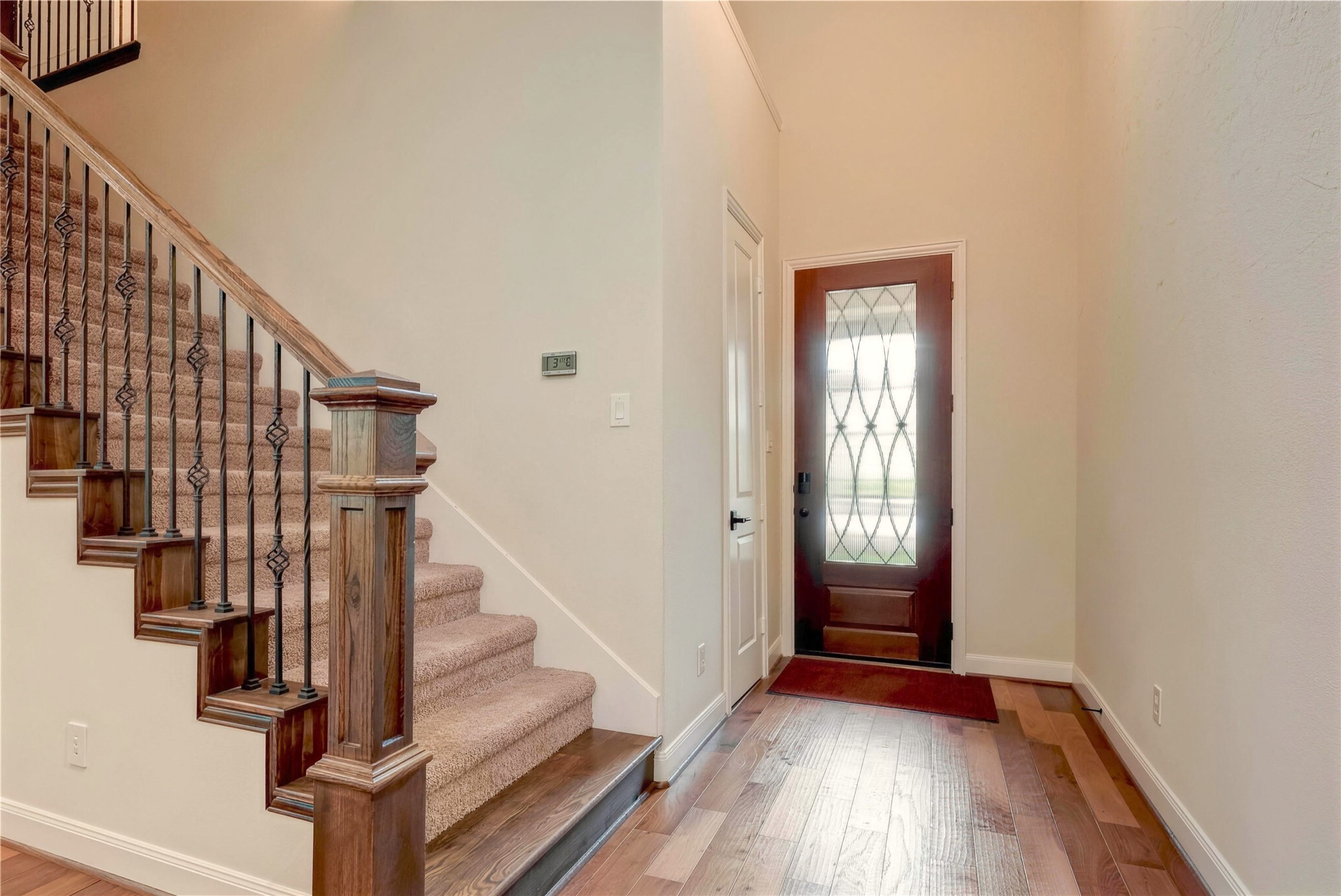 Inviting entryway featuring a stylish wooden staircase with wrought iron balusters and a decorative front door with glass insets, complemented by warm hardwood flooring.