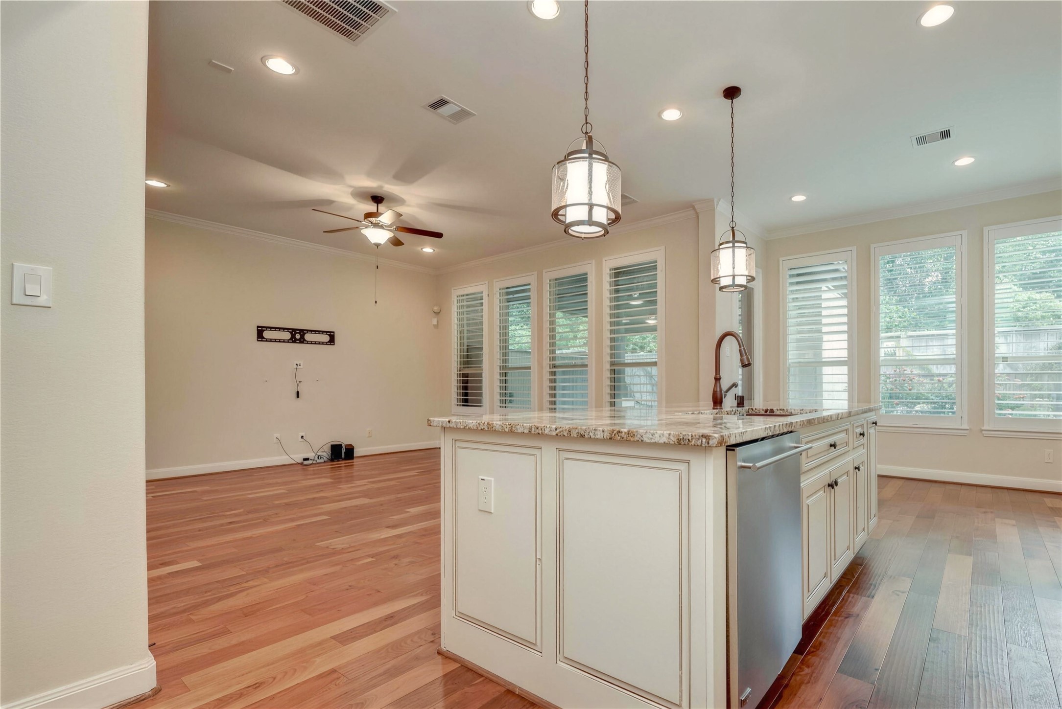 Spacious open-concept living area with elegant hardwood floors, featuring a modern kitchen island with granite countertops and stylish pendant lighting, complemented by large windows that fill the space with natural light.