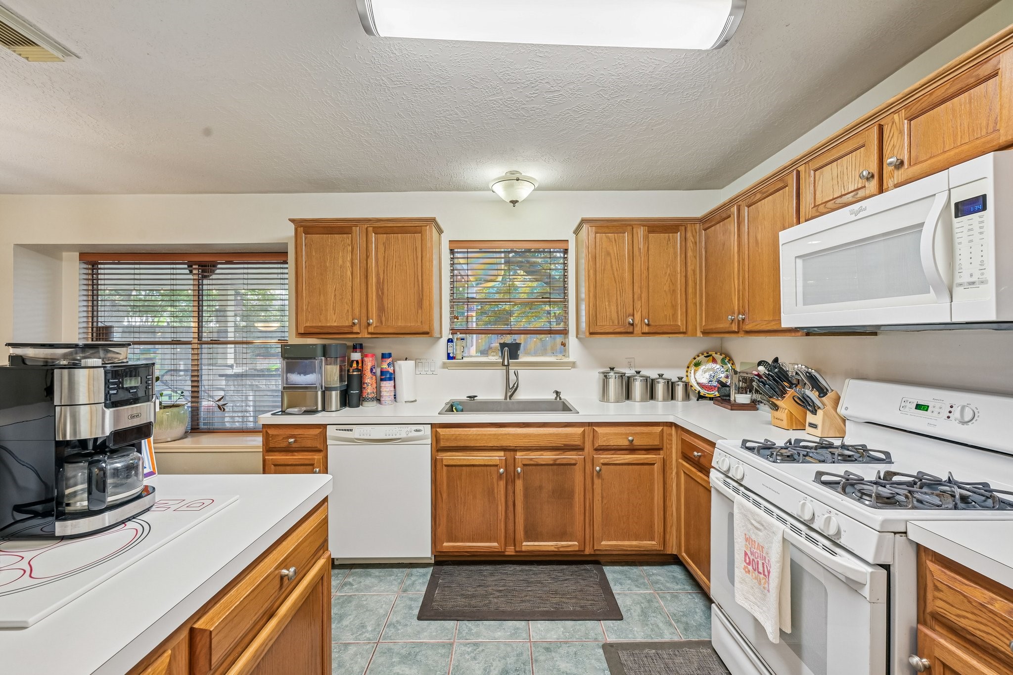 Spacious kitchen featuring solid wood cabinetry, gas cooktop and oven range, tile flooring, and ample counter space with garden window view.