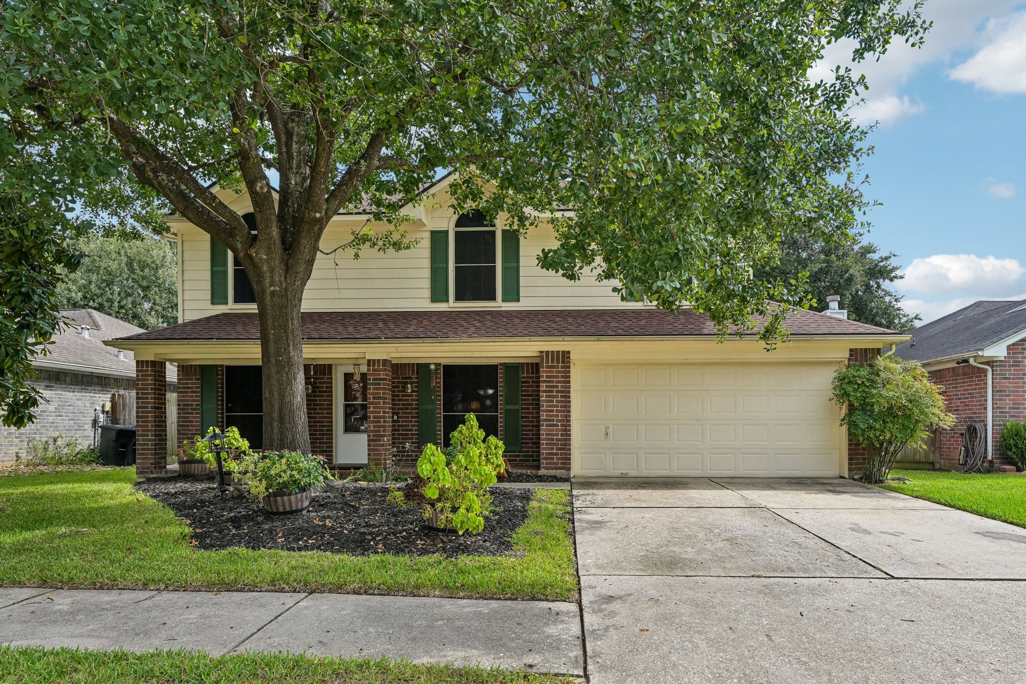 Classic two-story home featuring timeless brick and siding exterior, lush green lawn, mature shade tree, and an attached two-car garage. Classic two-story home featuring timeless brick and siding exterior, lush green lawn, mature shade tree, and an attached two-car garage.