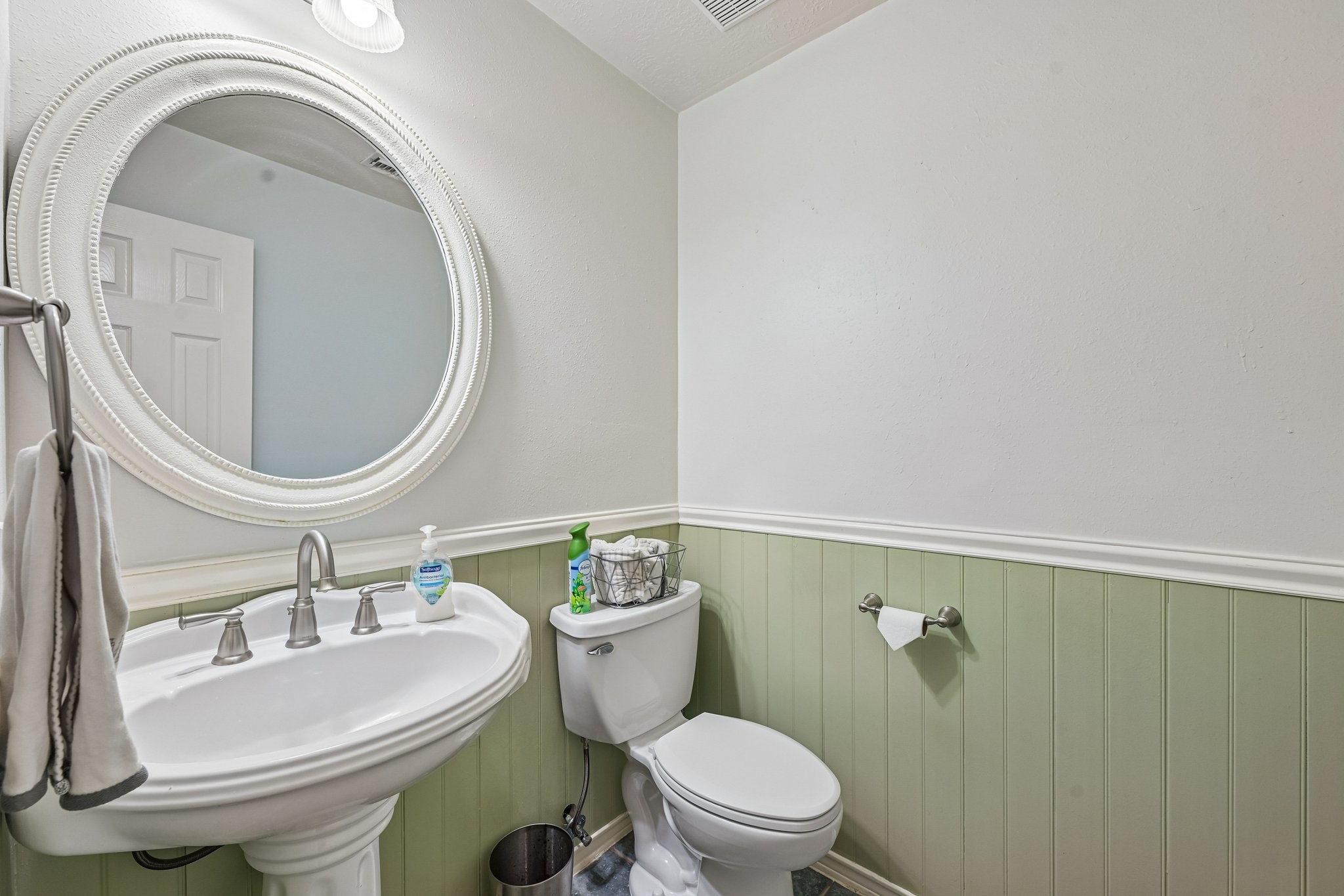 Downstairs half bath featuring classic sage green wainscoting, white pedestal sink, and decorative oval mirror.