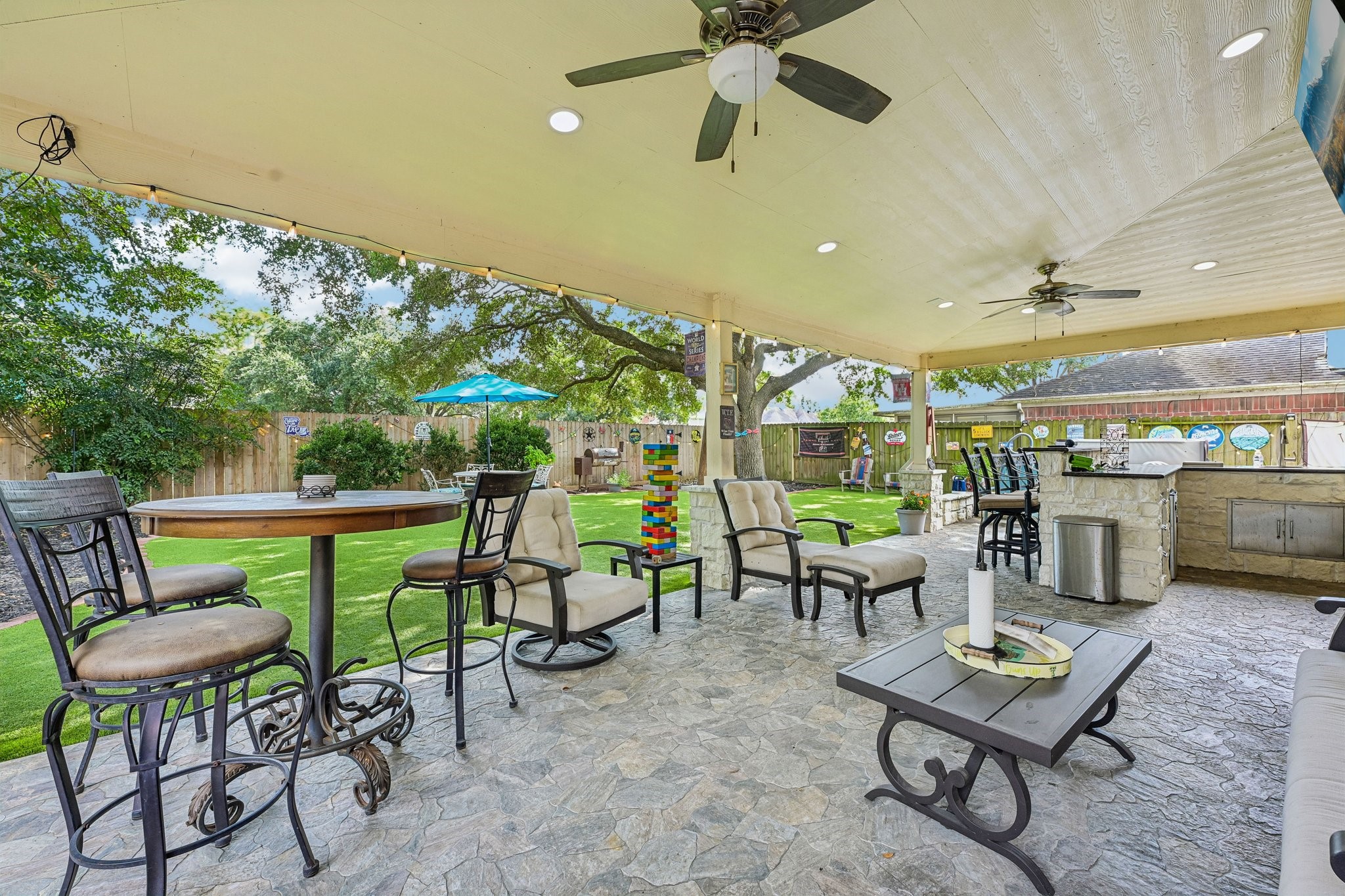 Impressive covered patio featuring stamped stone-look flooring, dual ceiling fans, recessed lighting, outdoor bar seating, and outdoor kitchen access.