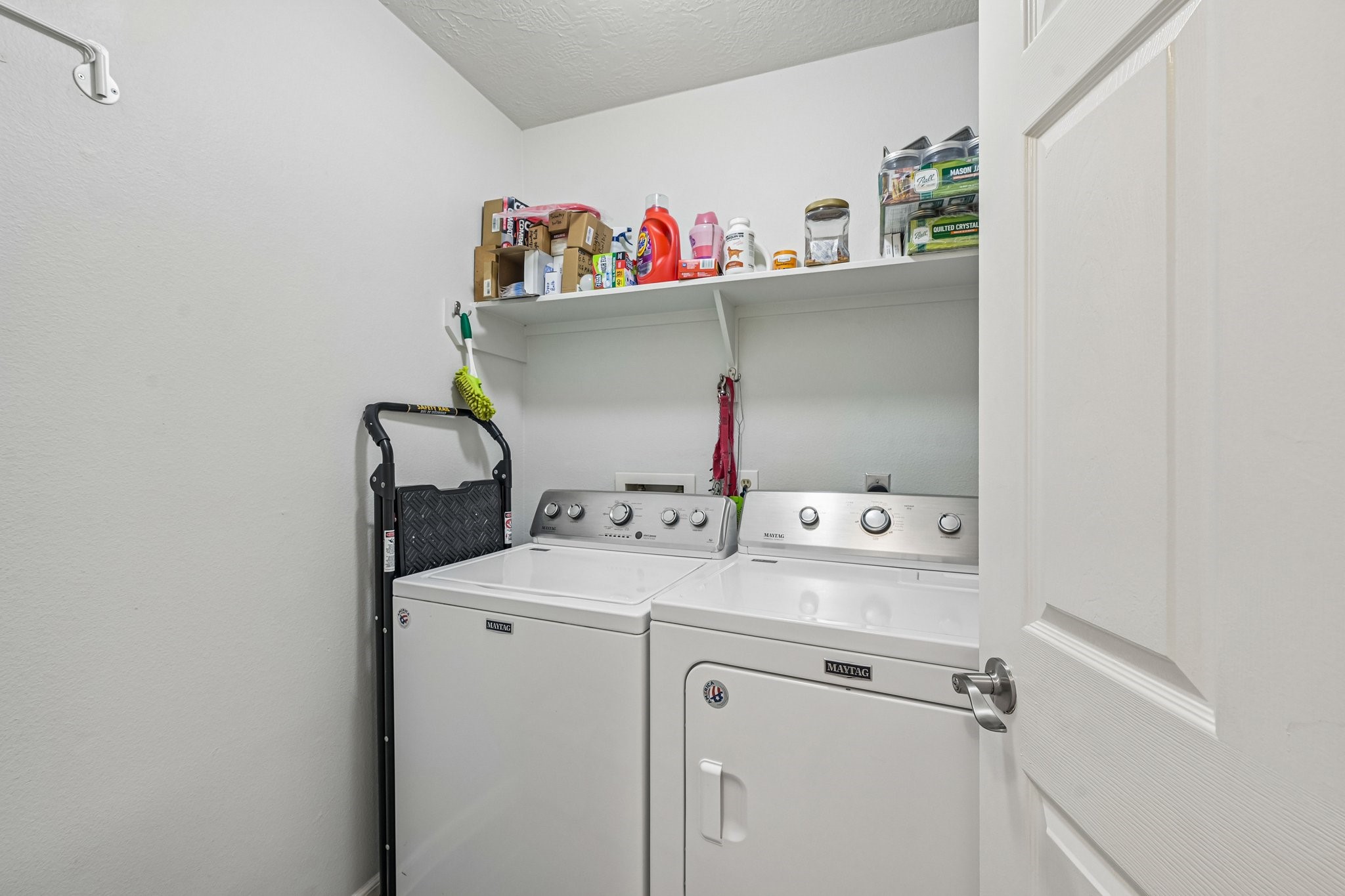 Dedicated indoor laundry room equipped with washer/dryer connections and overhead storage shelving.